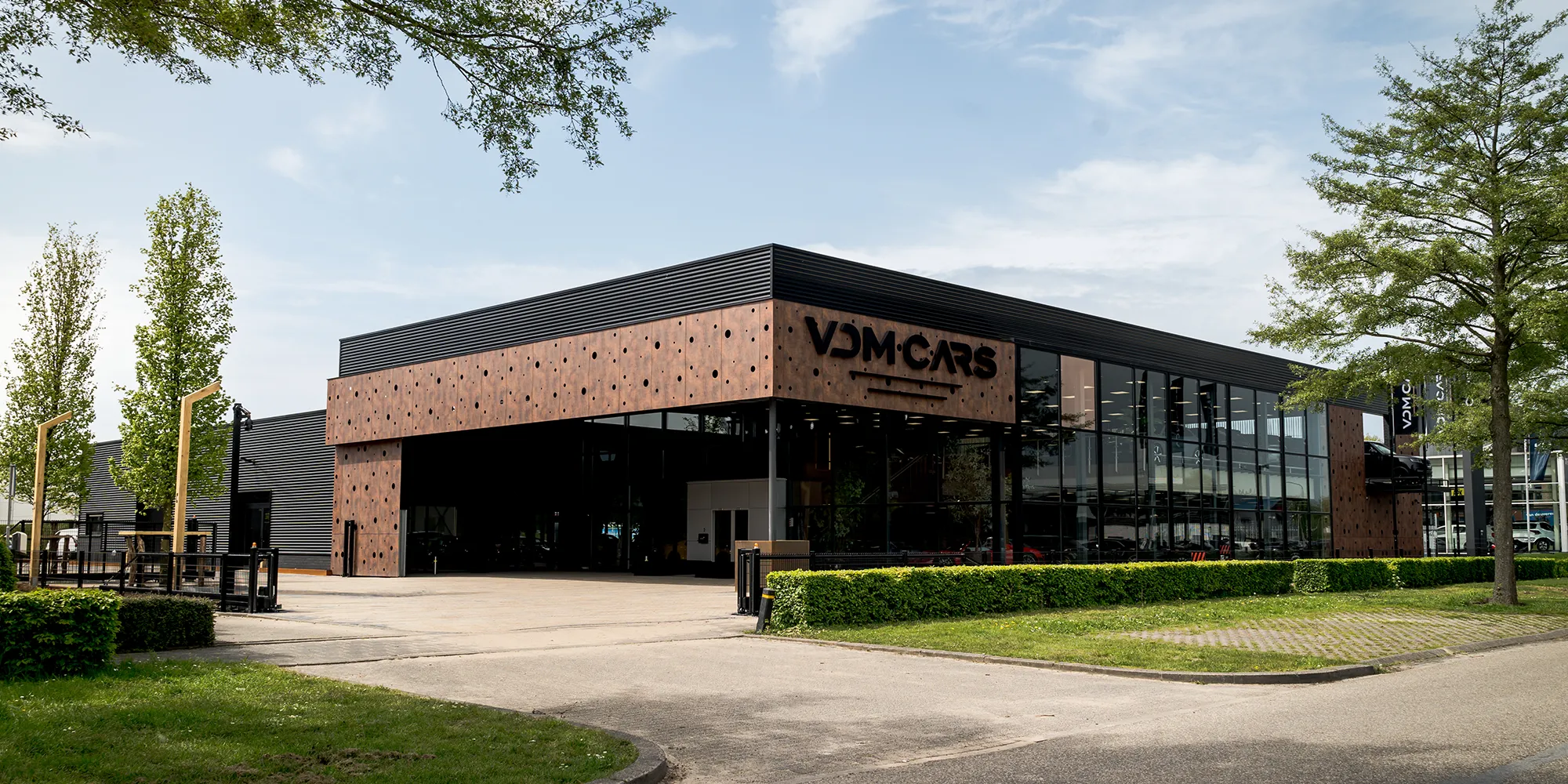 Buitenaanzicht van het VDM Cars gebouw met glazen gevel en showroomverlichting zichtbaar van buiten