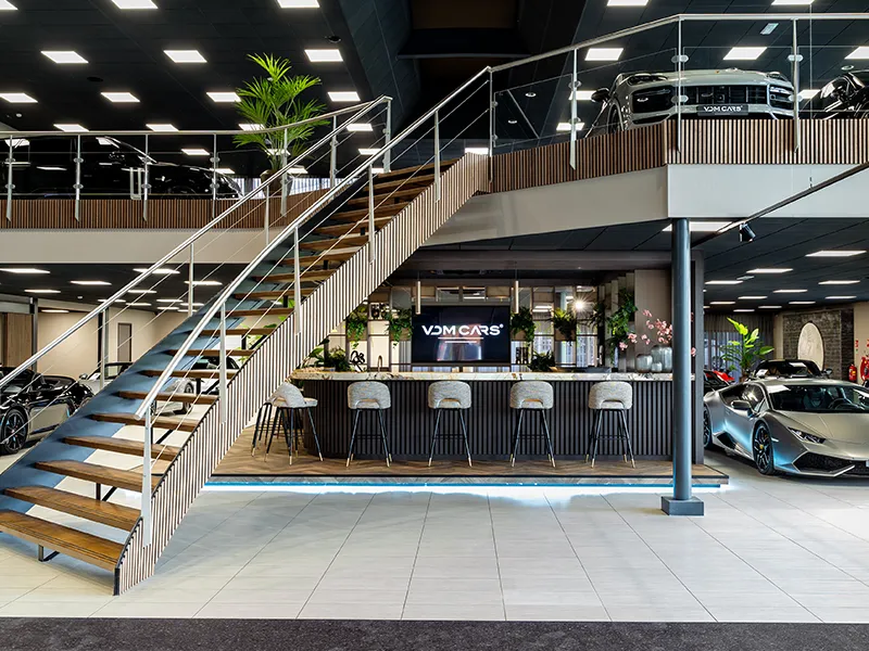 Tweeverdiepingen showroom van VDM Cars met trap, centrale balie en led-panelen boven Lamborghini en andere supercars