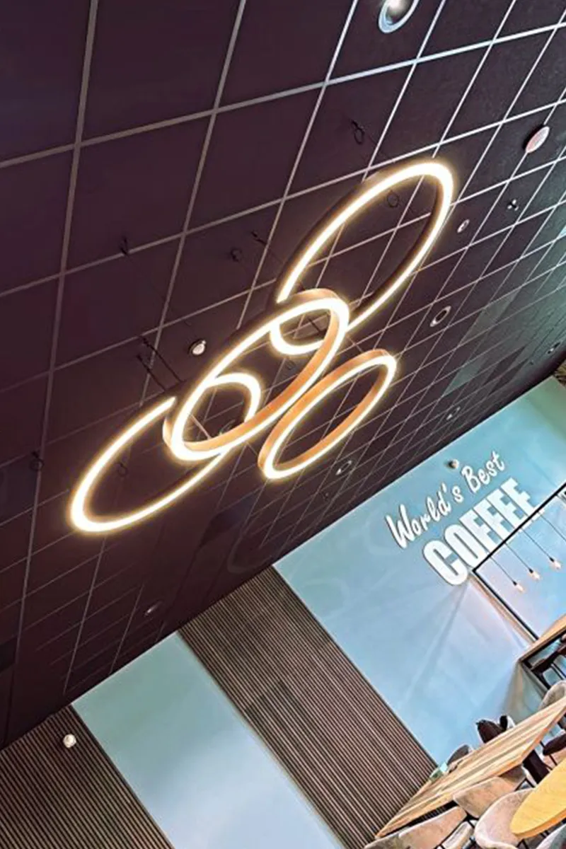 Verlichte LED-ringen aan donker plafond boven coffeecorner met World's Best Coffee wandtekst, gerealiseerd door Halo Lighting