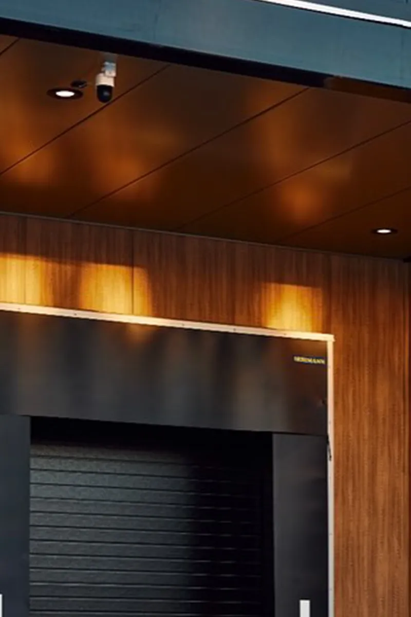 Warm verlicht houten plafond met inbouwspot boven donkere rolluikdeur in luxe kantooromgeving