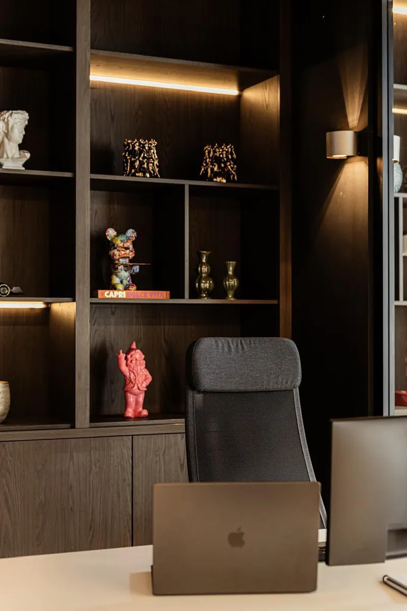 Donkere houten wandkast met indirecte LED-stripverlichting en up-down wandlamp in directiekantoor House of Capital