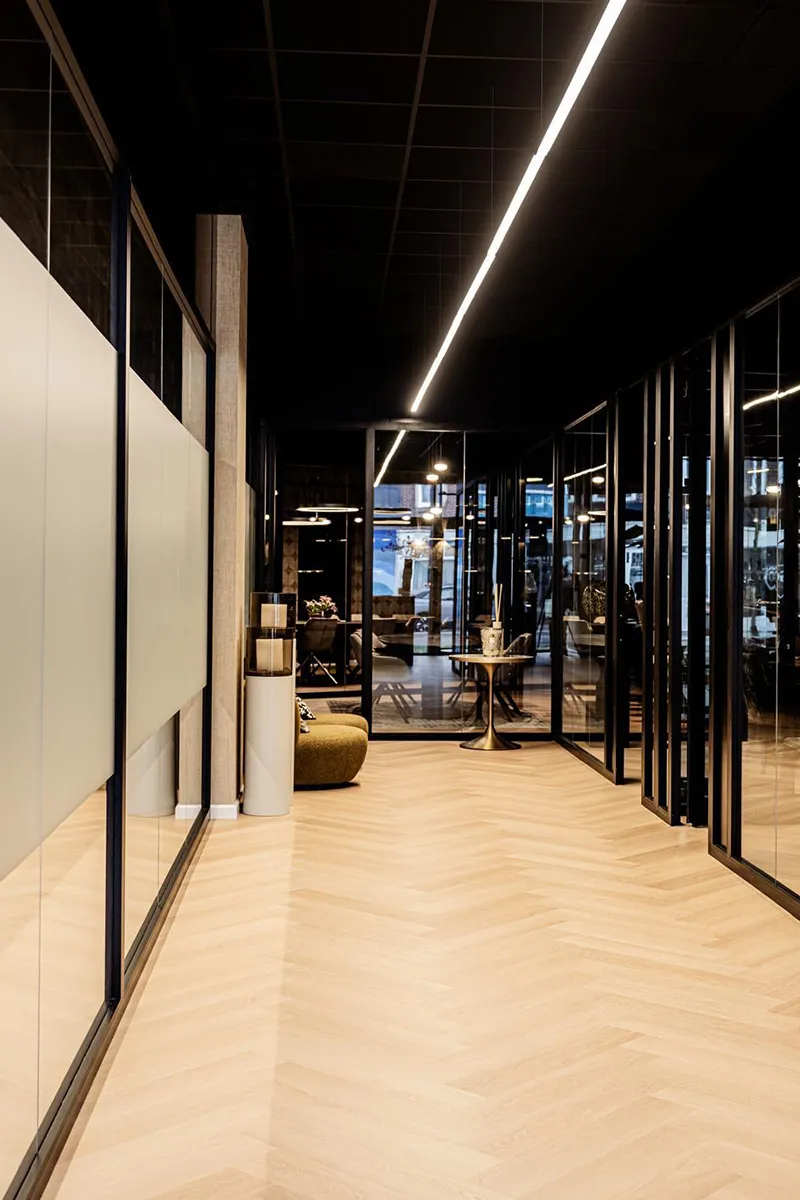 Lange gang bij House of Capital met lineaire LED-verlichting aan donker plafond en zwarte stalen glaswanden