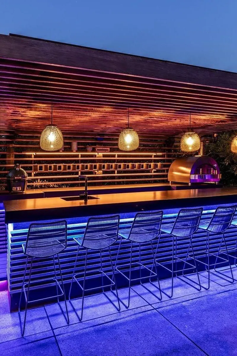 Buitenbar in de avond met blauwe LED-onderverlichting, gevlochten hanglampen en houten lamelwand