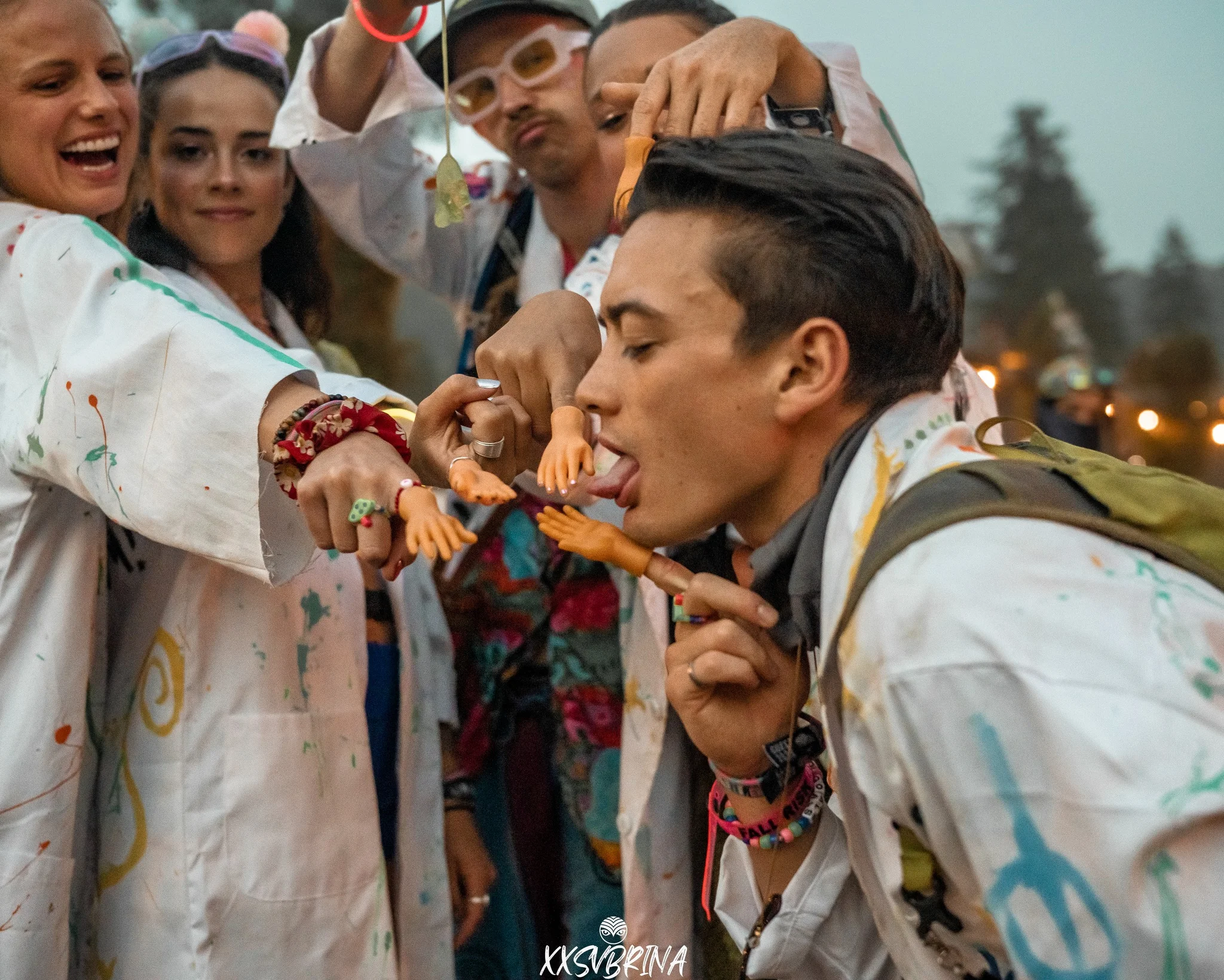 a group of friends at Shambhala 2023 in hand painted coats wearing tiny hands on their fingers and laughing