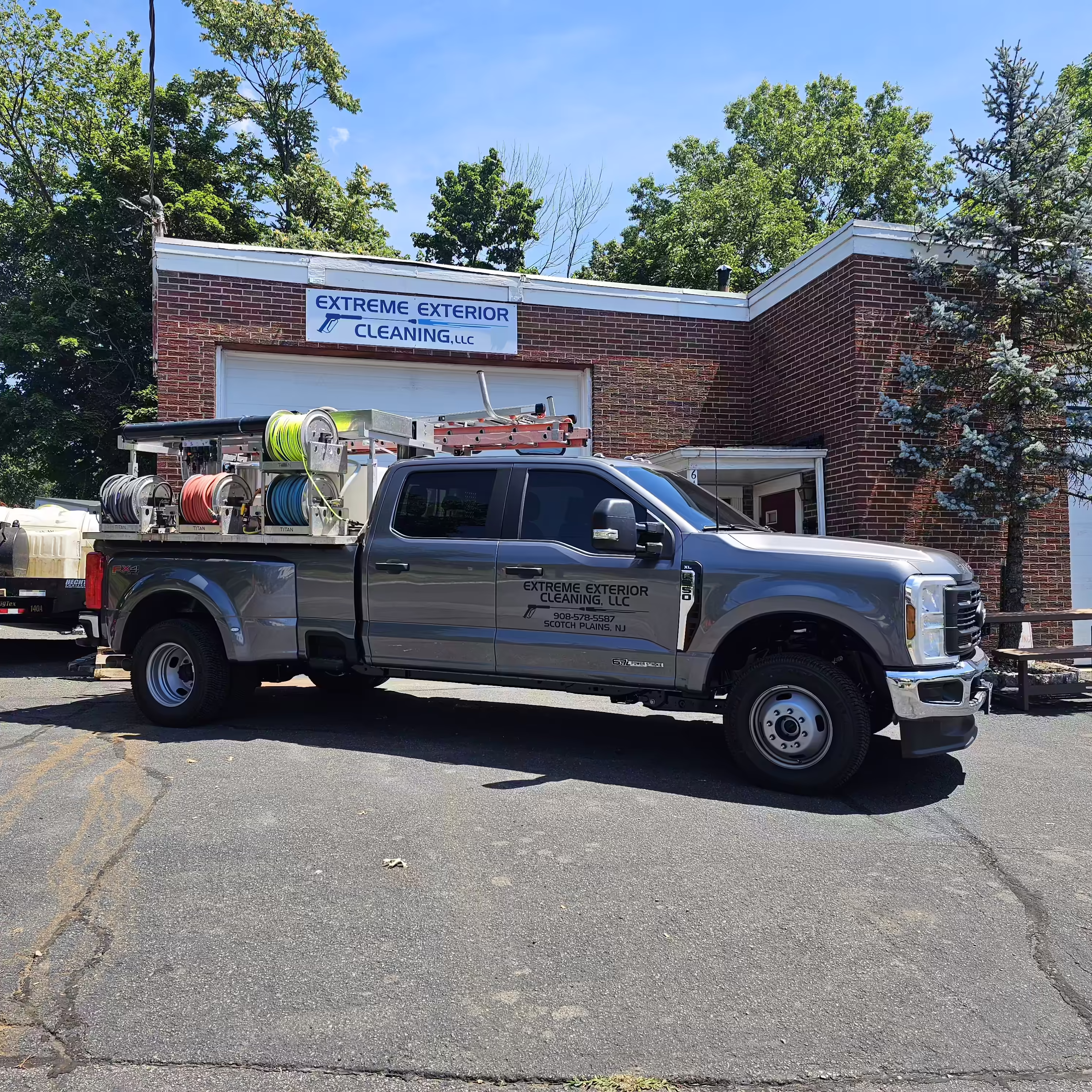Gray work truck with ladders and colorful hose reels parked in front of a brick building with sign 'Extreme Exterior Cleaning, LLC'.