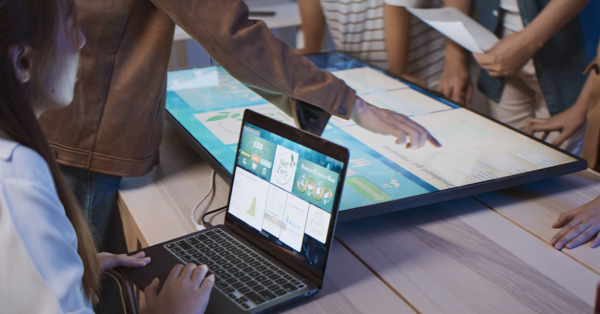 People collaborating around a touchscreen table and a laptop displaying data.
