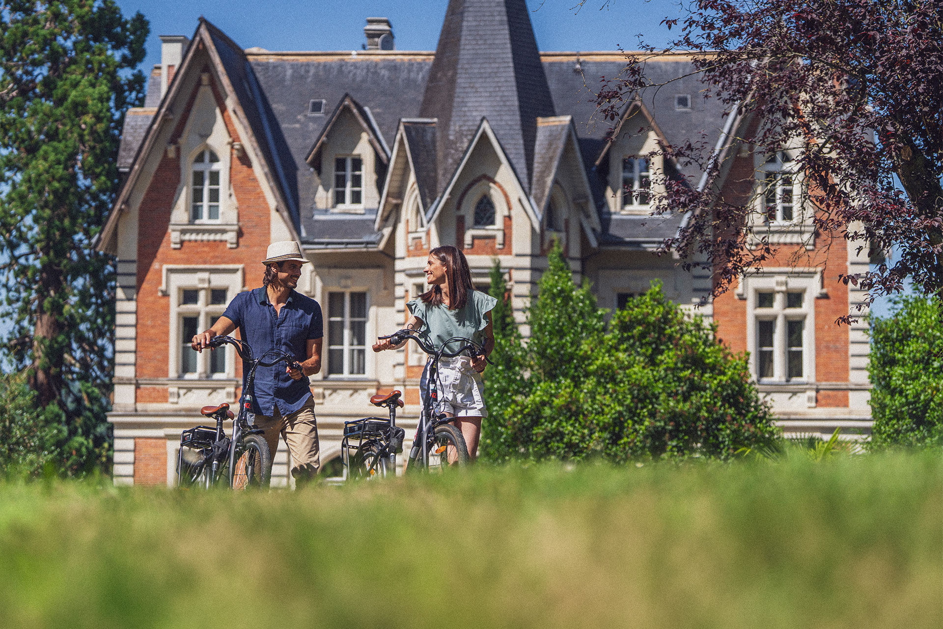 Un couple à vélo devant le Château des Forges