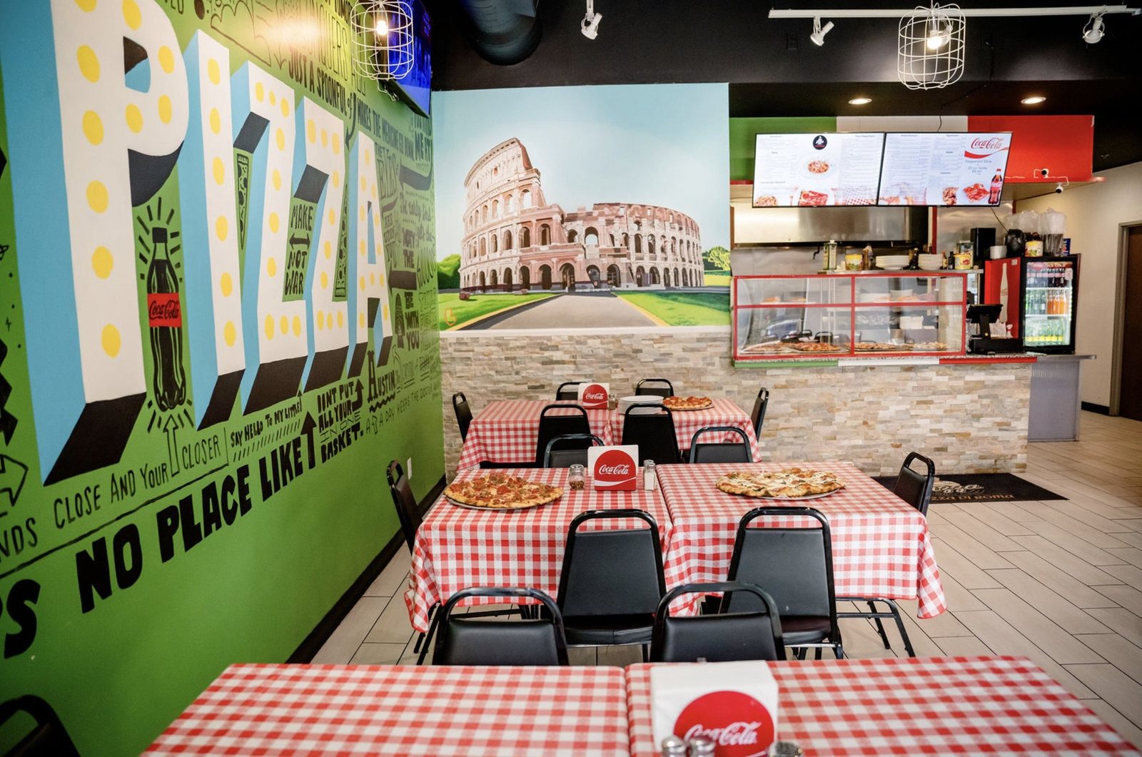 Pizza Di Roma's dining room in Austin: a PIZZA mural, Colosseum painting, checkered tablecloths and menu boards