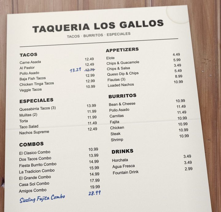 A photo of a paper menu with prices crossed out and written in by hand