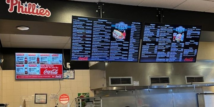 Two dark menu boards and a specials screen over the kitchen at Big Tony's West Philly Steaks