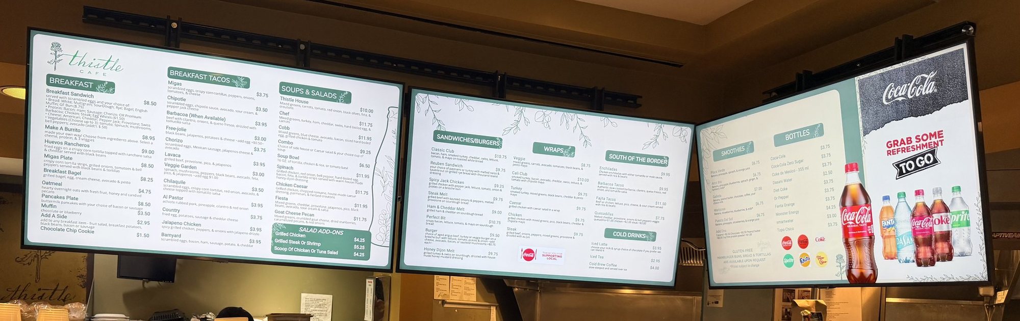 Three light green menu boards at Thistle Cafe: breakfast, sandwiches and wraps, and a drinks board