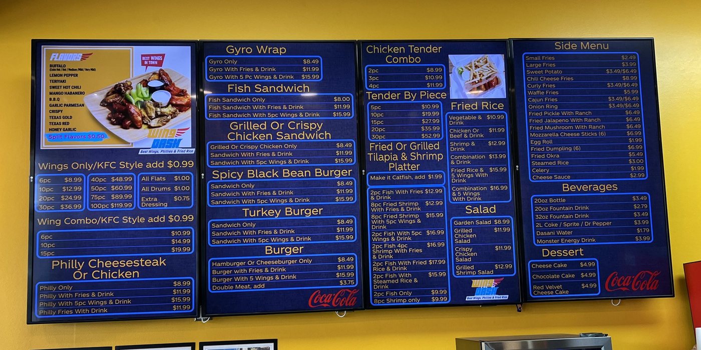 Four navy menu boards with gold type on a yellow wall at Wing Dash