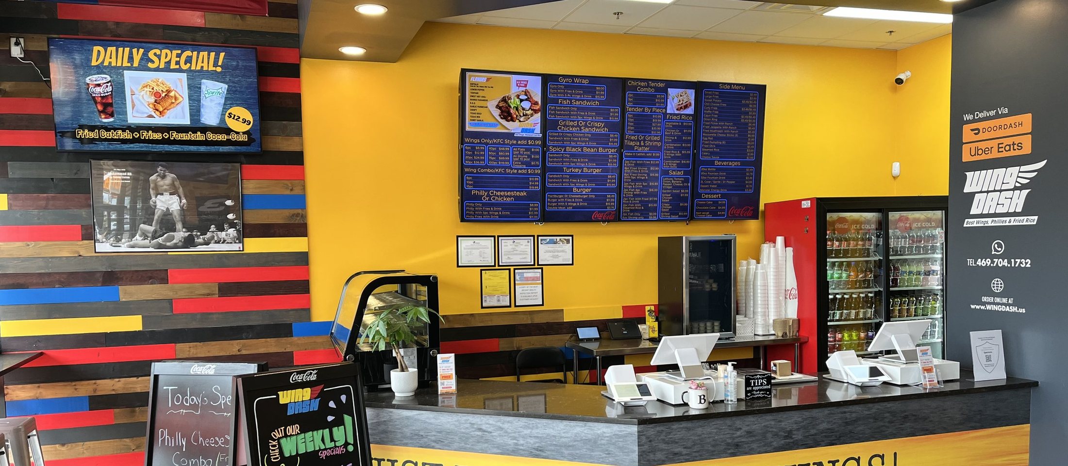 The Wing Dash counter in Dallas: four menu boards on a yellow wall and a Daily Special screen on the wall beside it
