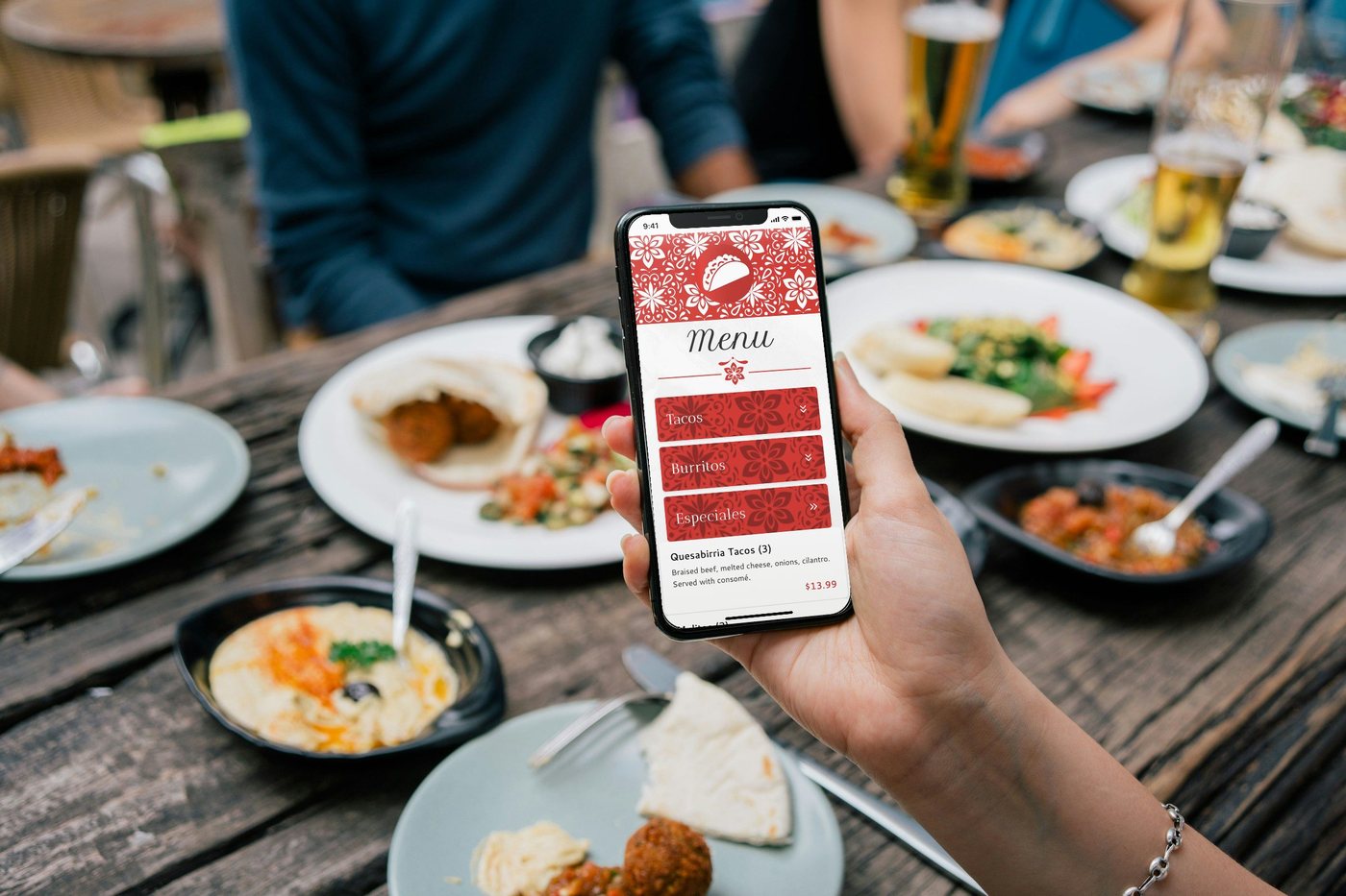 A guest holding a phone with the taqueria's QR menu over a table of shared plates