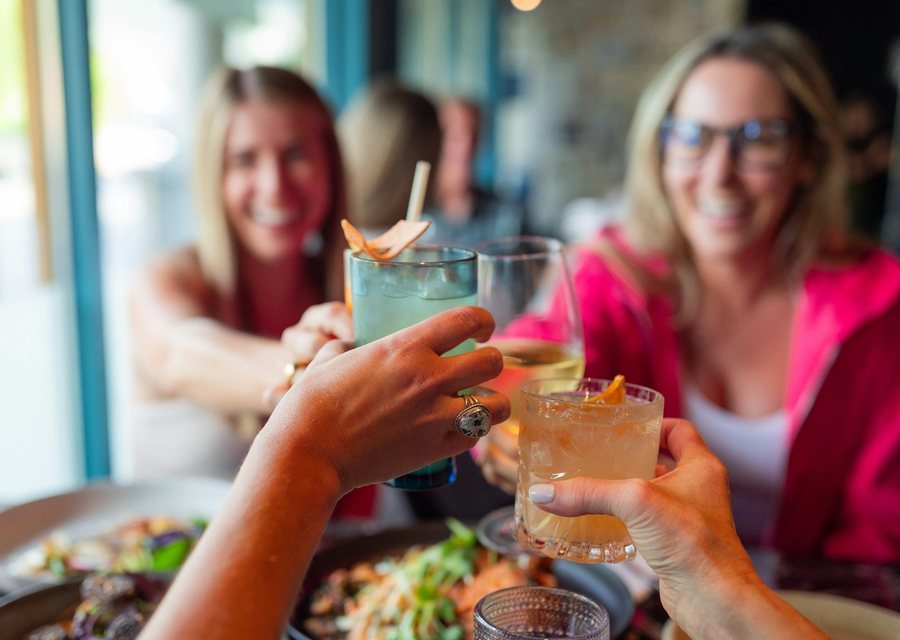 Friends clinking cocktails over shared plates at happy hour