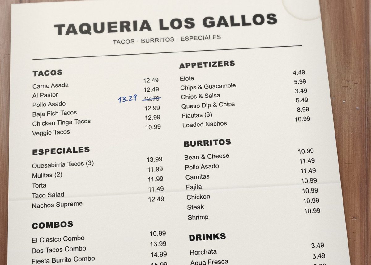 A photo of a paper taqueria menu on a wooden table: tacos, appetizers, especiales and burritos with prices