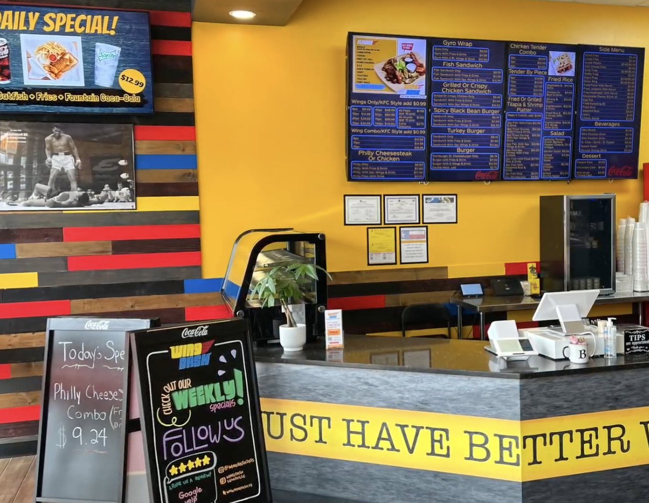 The Wing Dash counter in Dallas, with menu boards on a yellow wall and a Daily Special screen