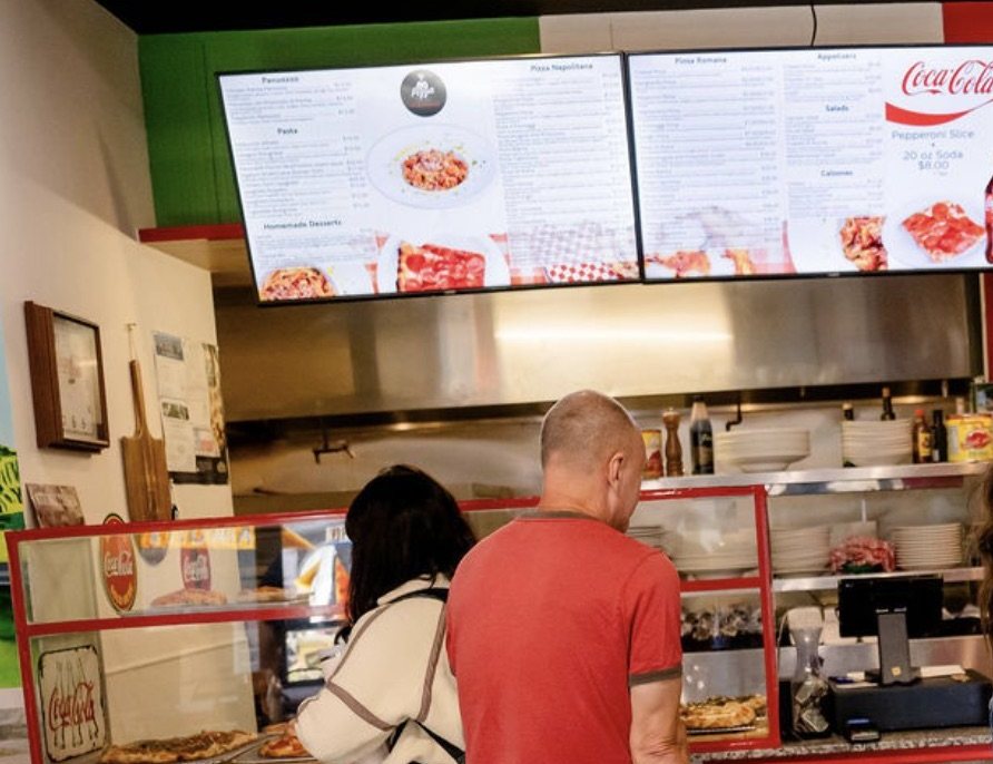Two guests order at the Pizza Di Roma counter under its two menu boards