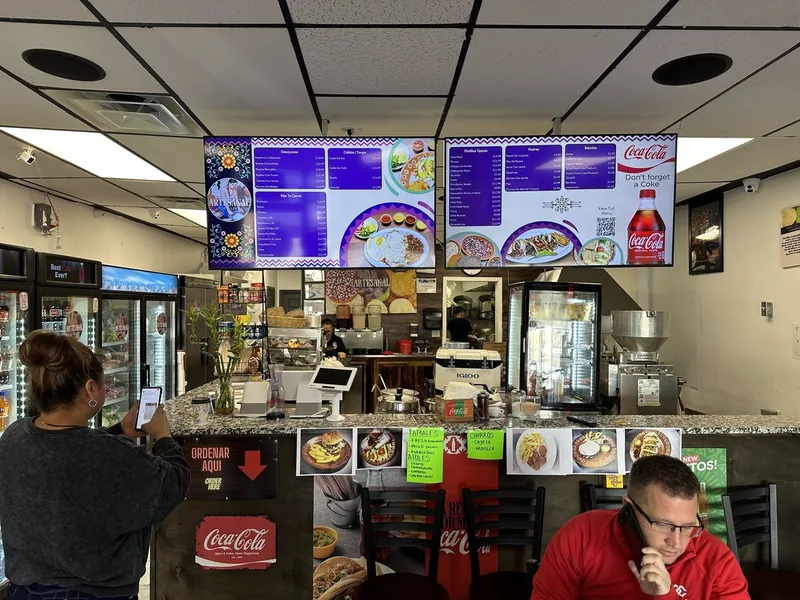 Guests at the counter of Artesanal Tortilleria in San Antonio, under two purple menu boards