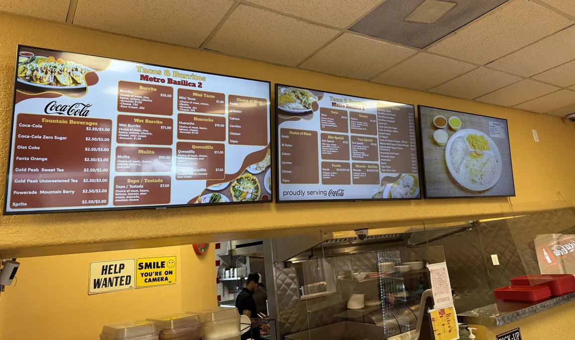 The menu boards at Tacos & Burritos Metro Basilica 2, with a food photo on the third screen
