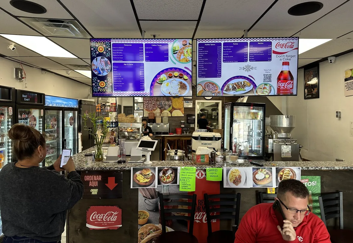 A guest takes a phone photo of the two purple menu boards over the counter at Artesanal Tortilleria in San Antonio