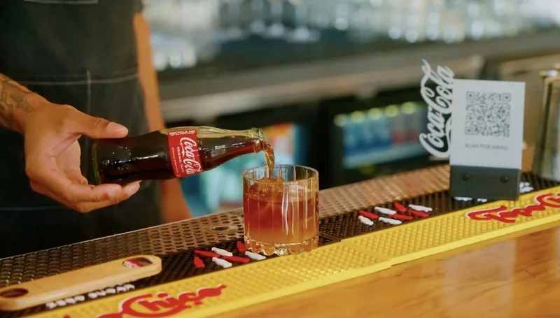A printed Scan for menu QR code stand on the bar at Verbena in Austin, beside a drink being poured
