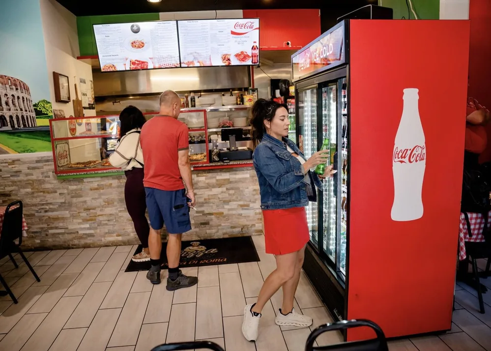 Guests ordering at the counter of Pizza Di Roma in Austin, under two menu boards, next to a drinks cooler