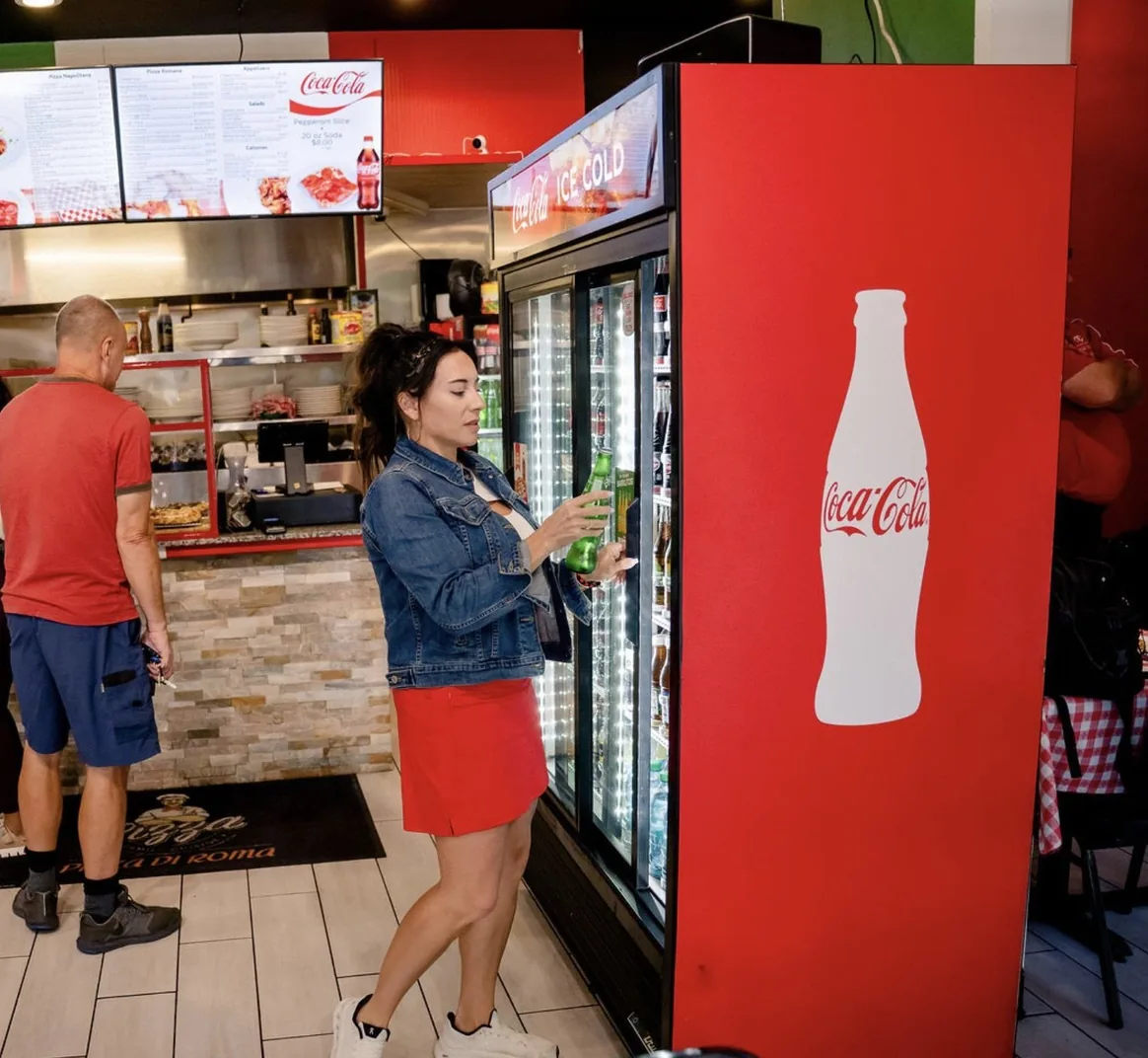 A guest takes a drink from the cooler at Pizza Di Roma while another orders under the menu boards