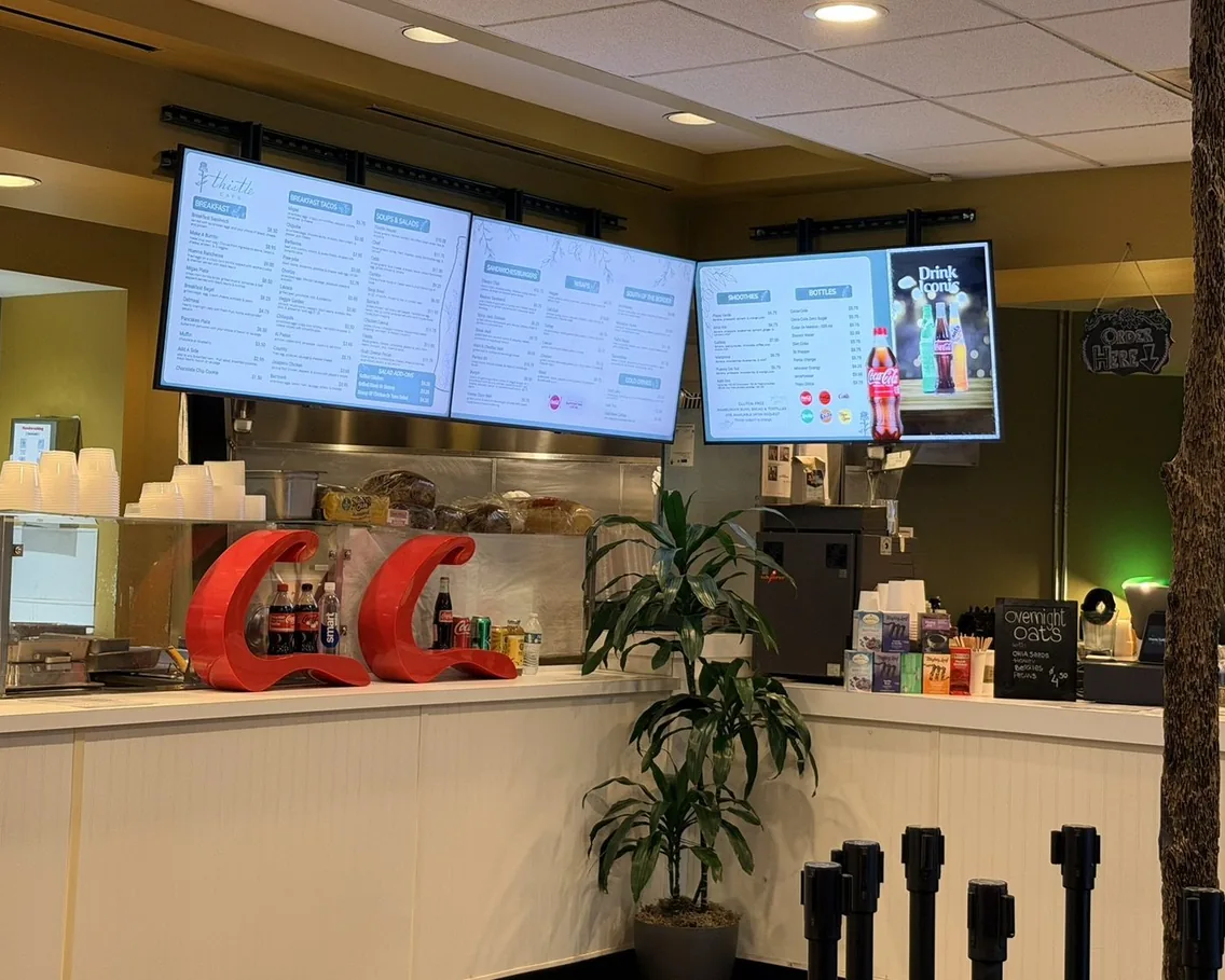 Three bright menu boards over the counter at Thistle Cafe in Austin: breakfast, sandwiches and a drinks board