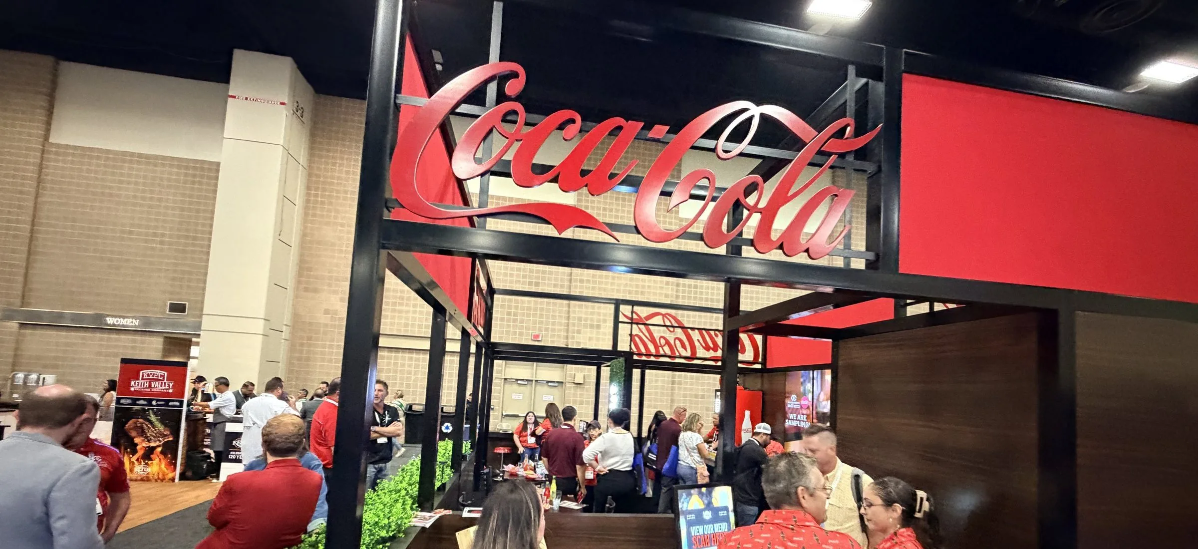 The Coca-Cola sign over the booth entrance at the Texas Restaurant Association Show 2026, with staff in red shirts