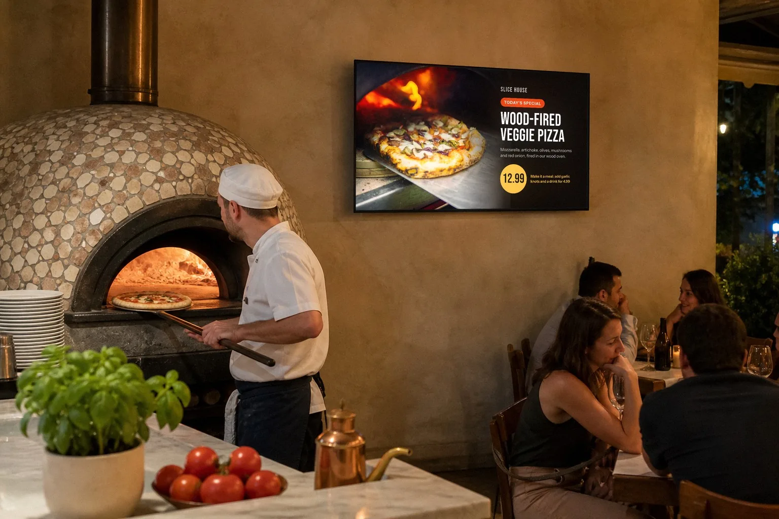 Illustration of a wood-fired pizzeria: a cook slides a pizza into the oven beside a TV showing a veggie pizza special with a photo and a price, while guests eat at their tables