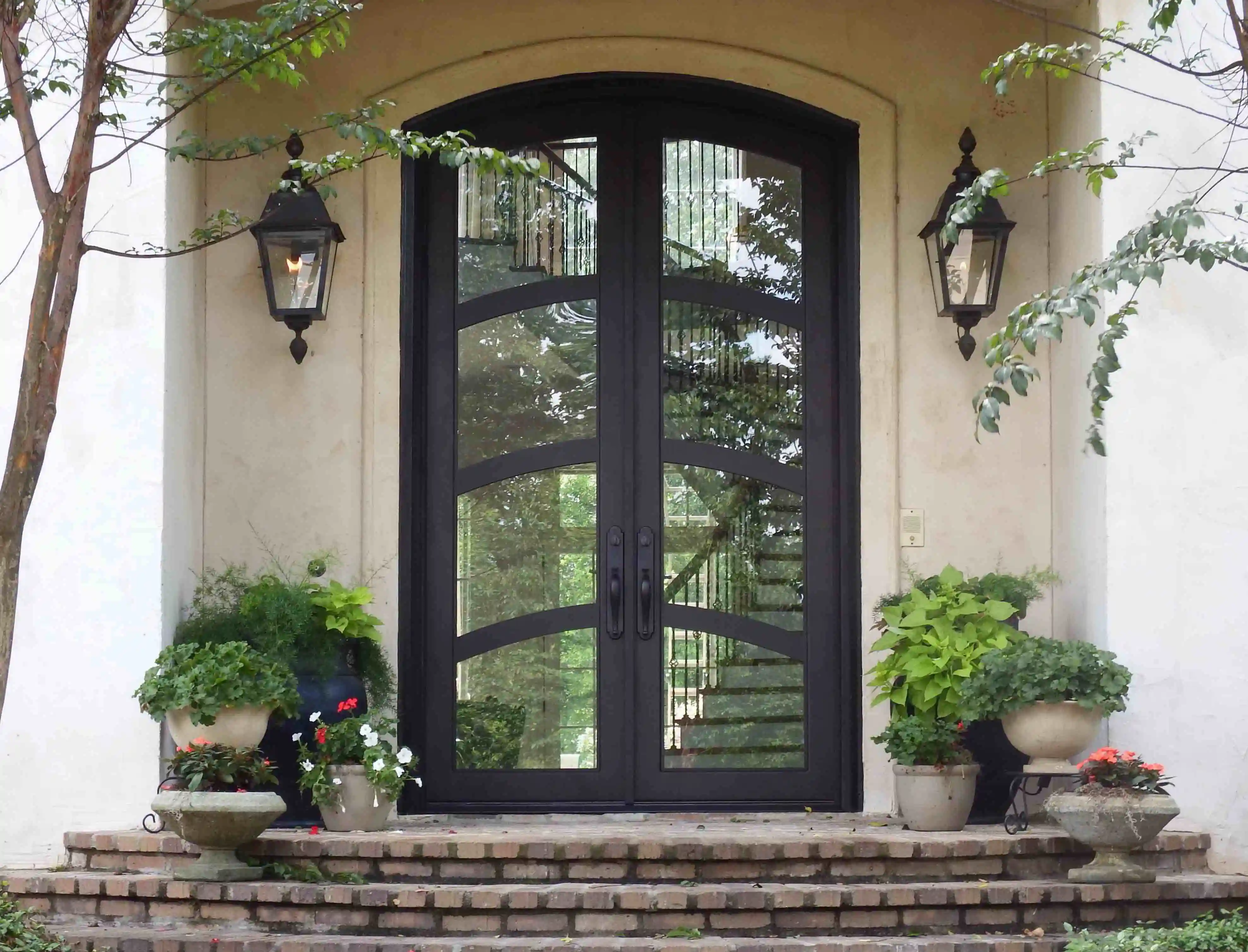 a black iron double entry door with 6 panes of arched glass on each door at the front of stucco house