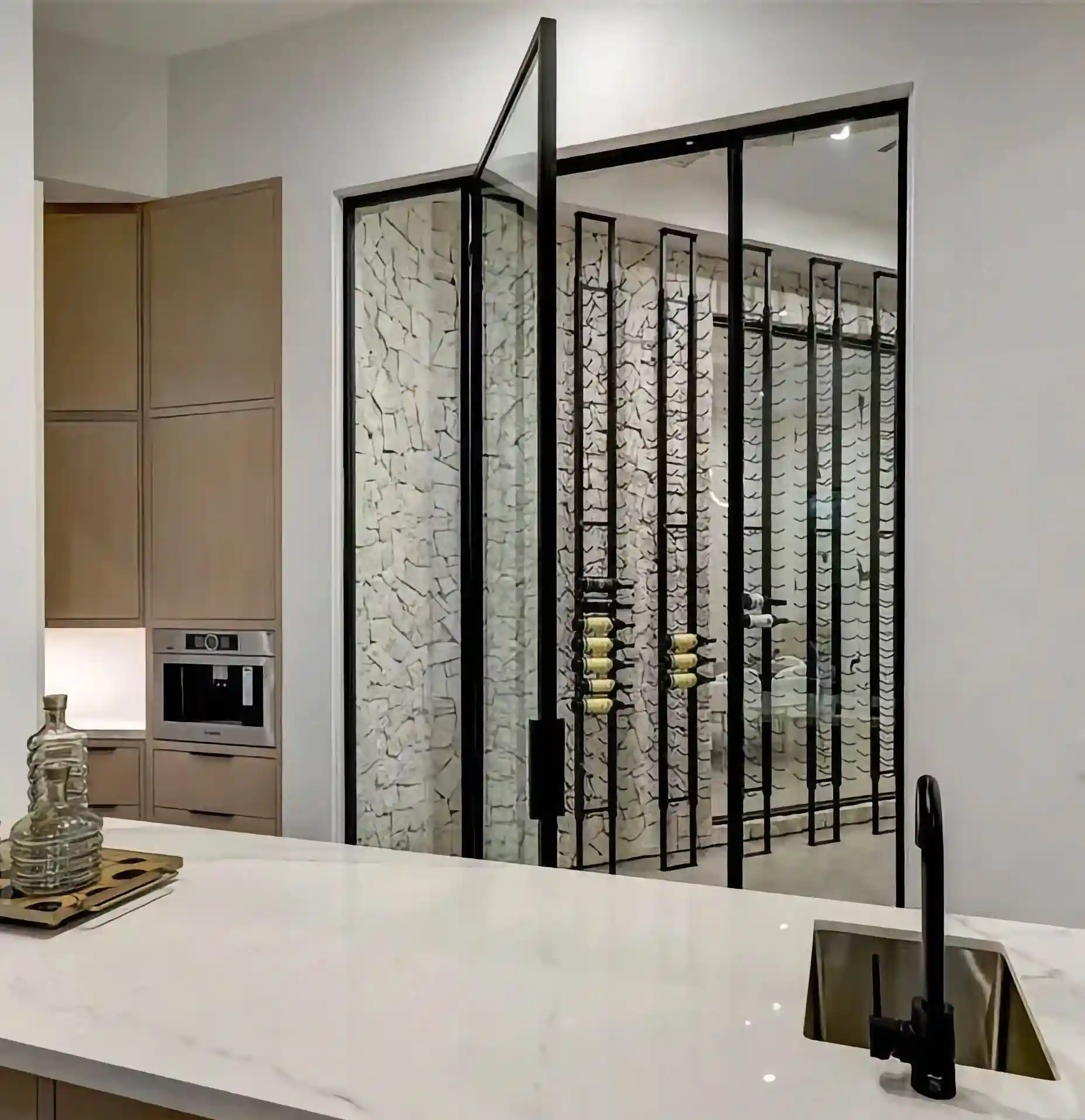 the inside of a home, looking over a stone countertop to a all glass and black iron door opening to outside 