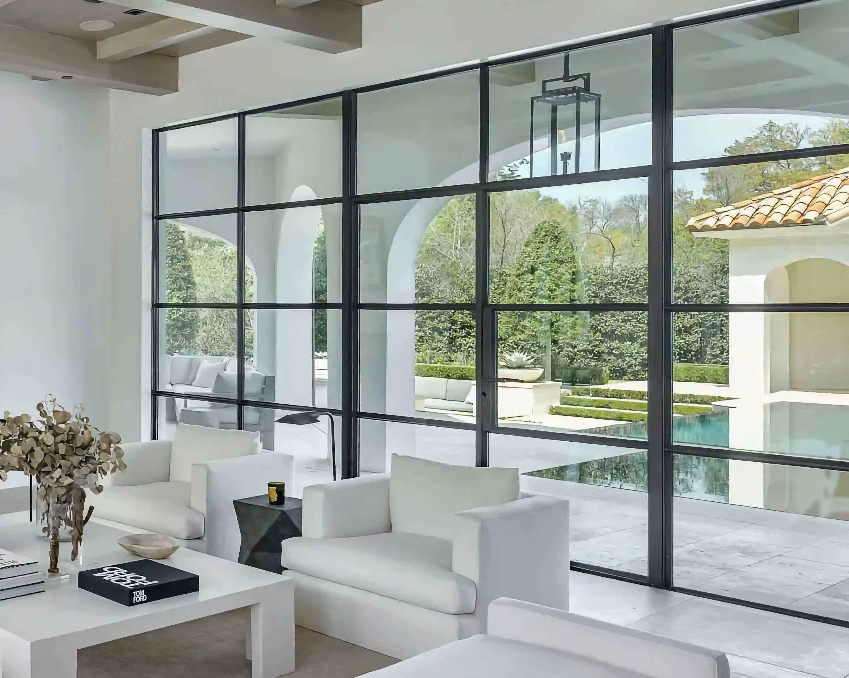 in the living room of a modern home, looking over furniture to a large glass and black iron wall looking over the back yard