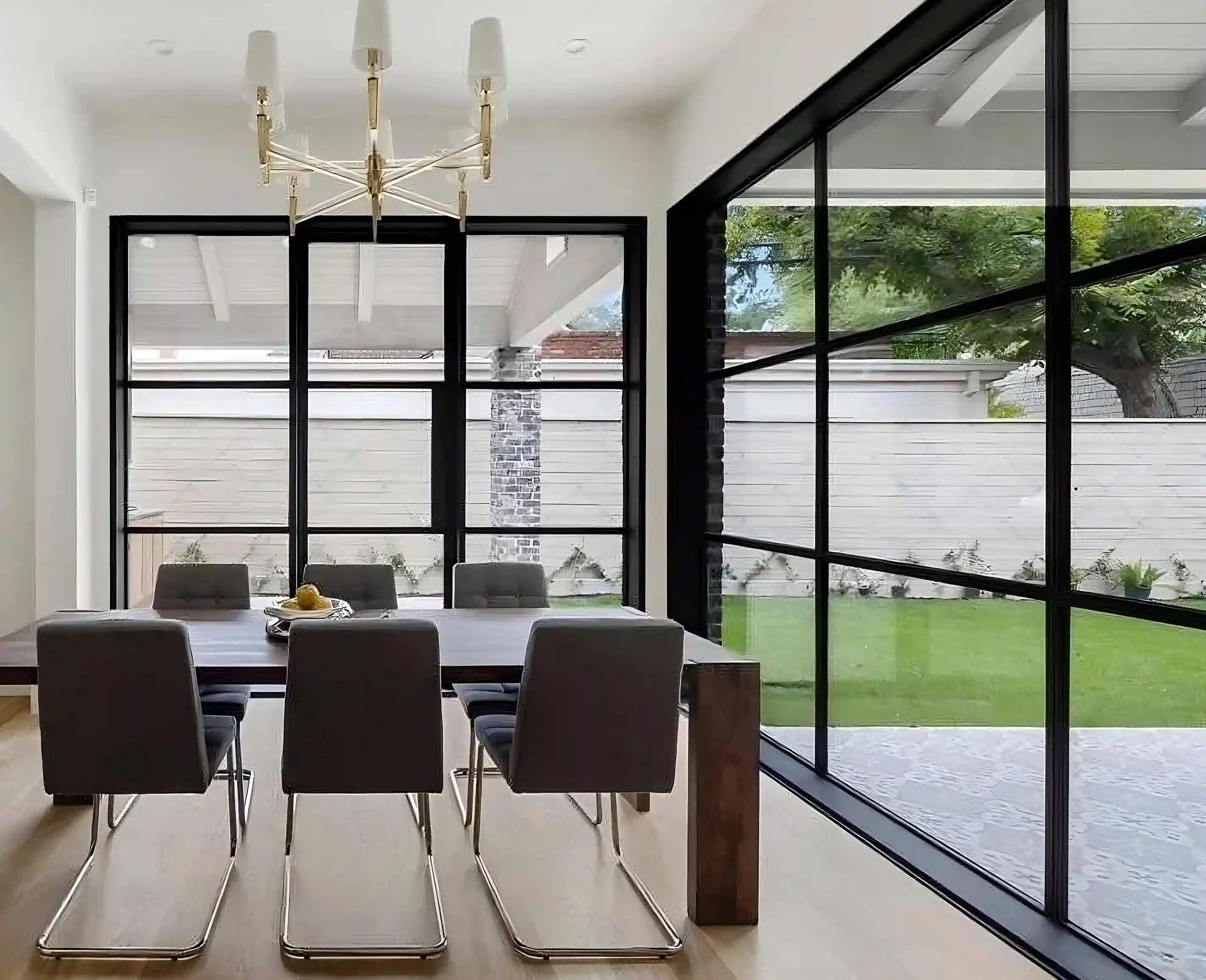 in the office/ dining room of a modern home, looking over furniture to a large glass and black iron wall in the back and to the right