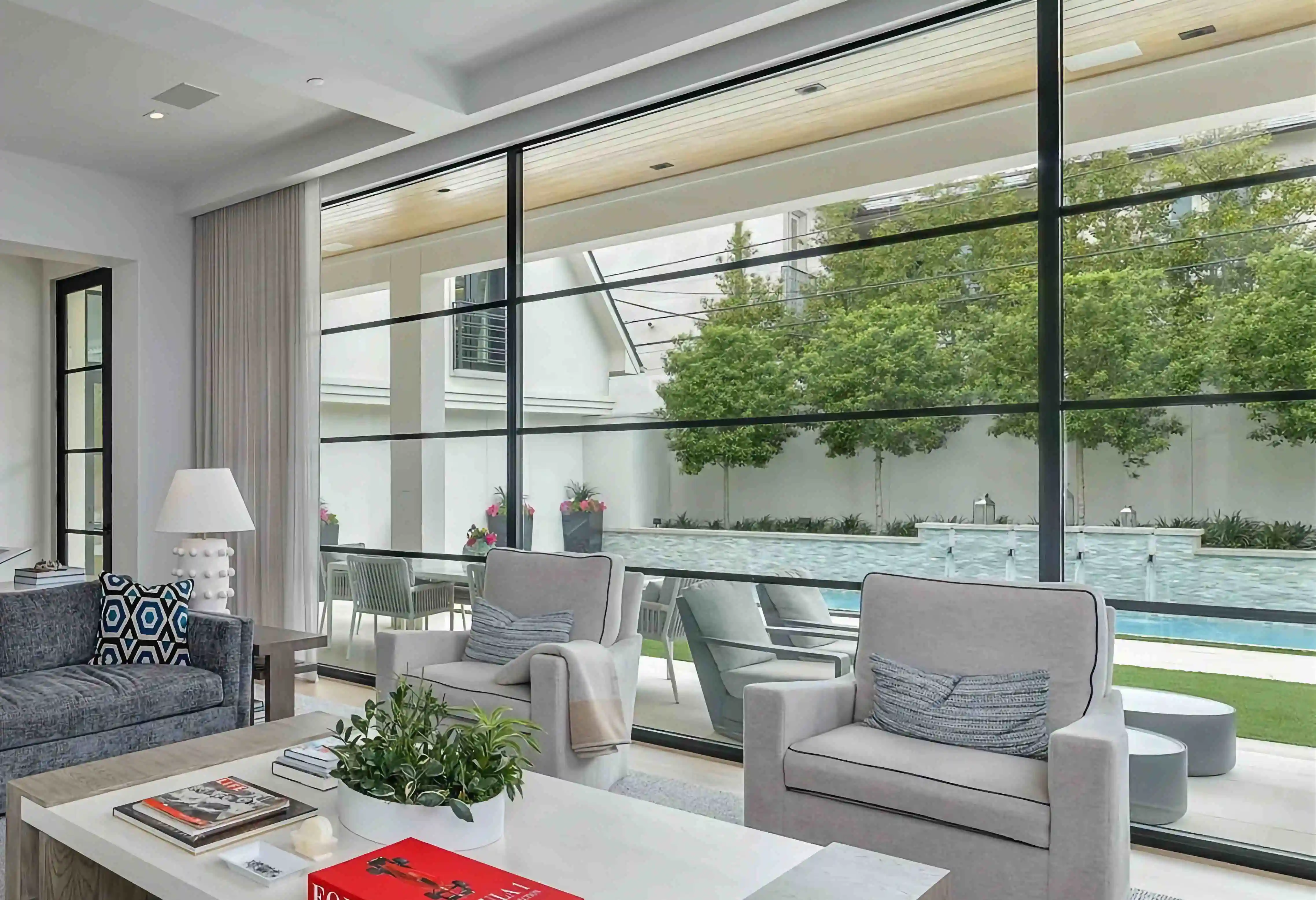 in the living room of a modern home, looking over furniture to a large glass and black iron wall looking over the back yard