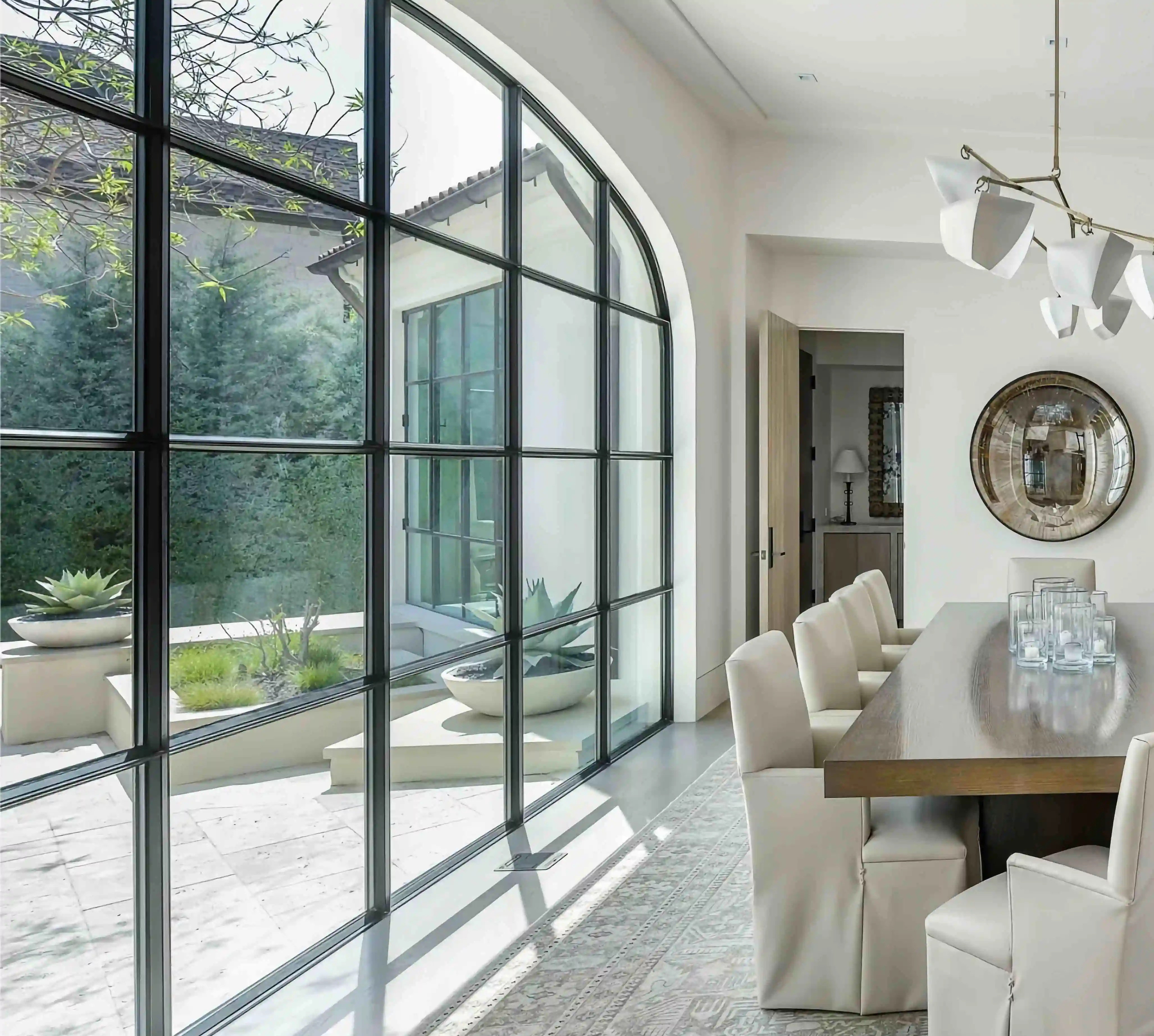 inside a home with a large arched glass and black iron wall on the left and a dining table on the right