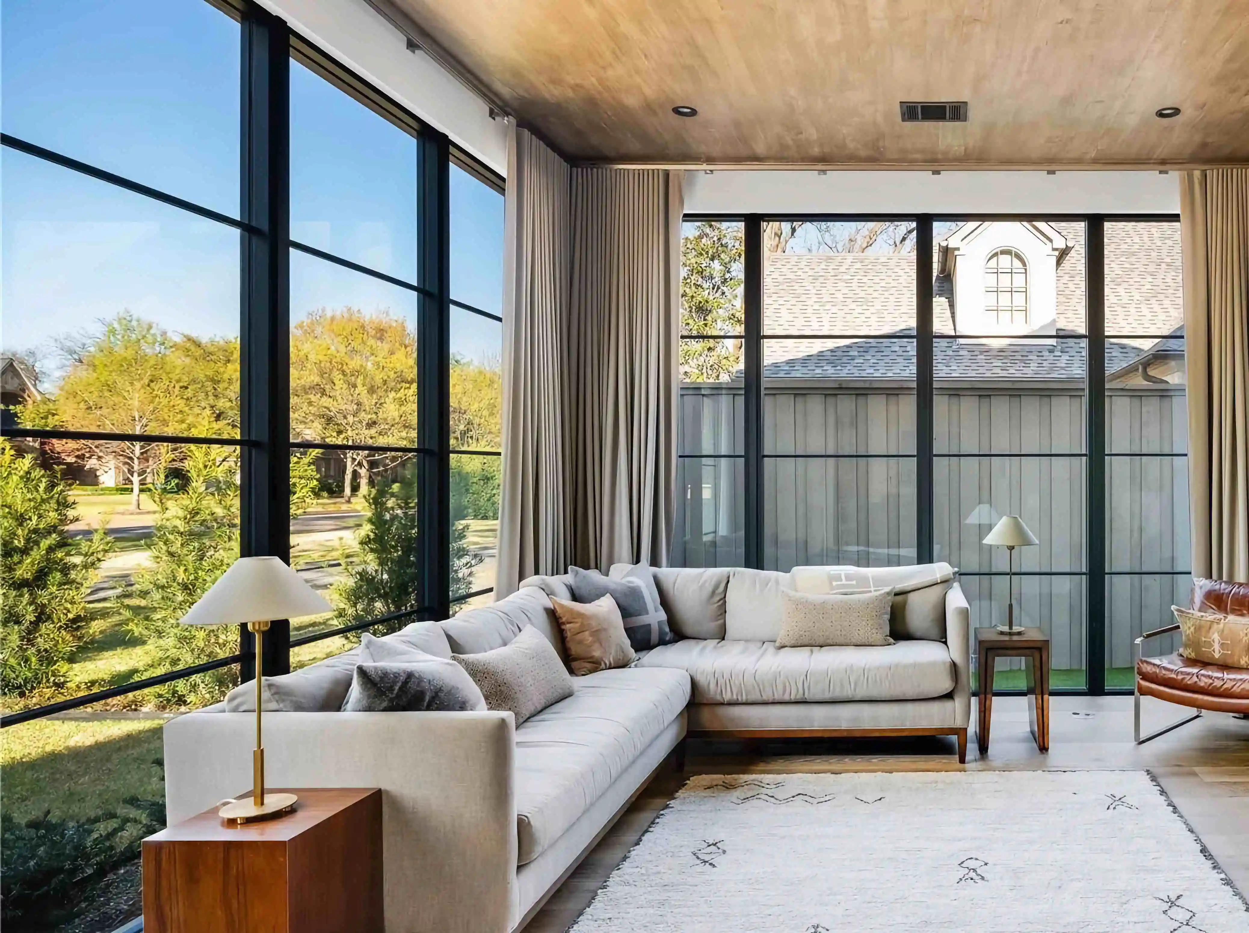 in the living room of a modern home, looking over furniture to a large glass and black iron wall looking over the back yard