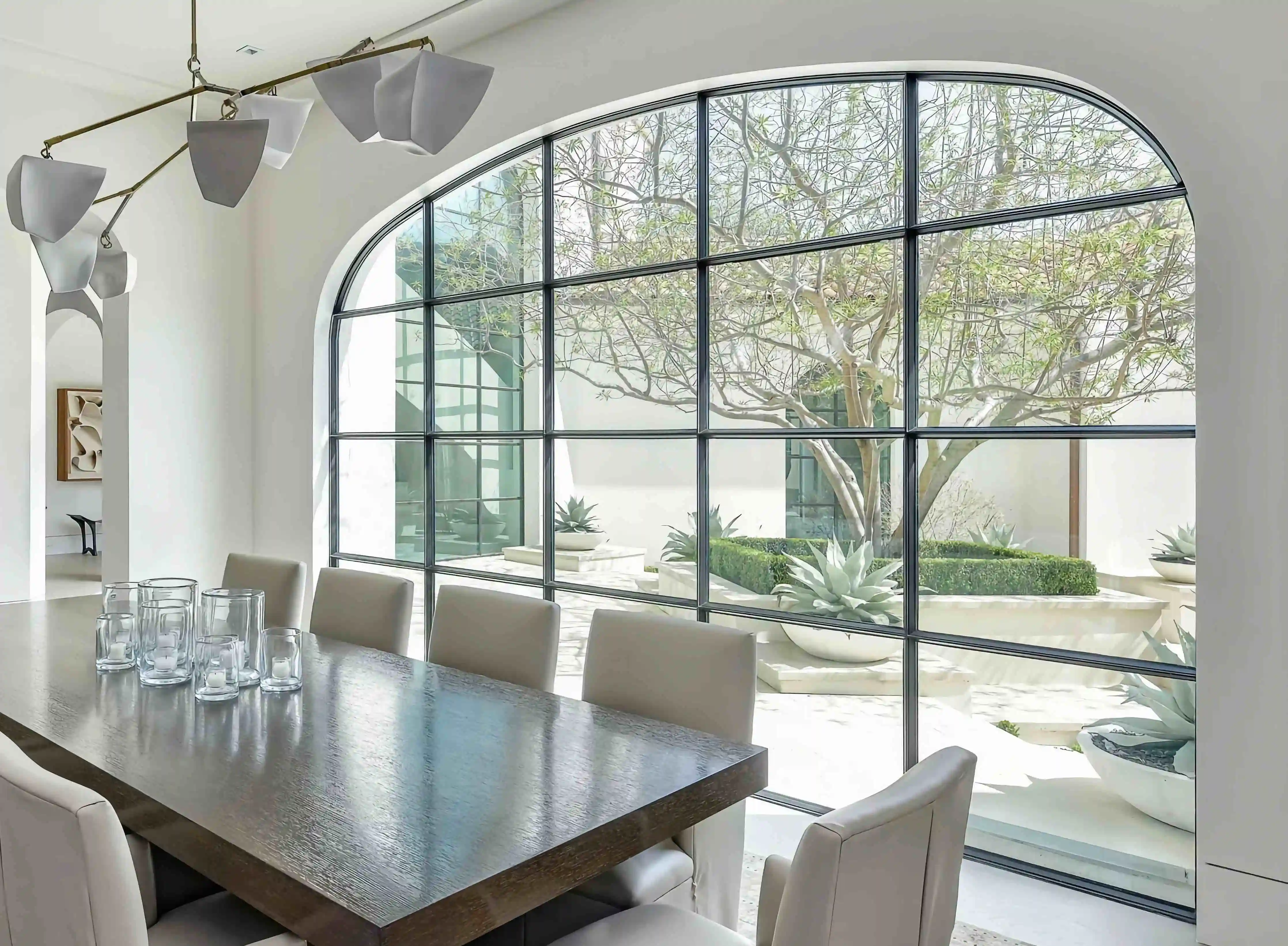 in the dining room of a modern home, looking over furniture to a large glass and black iron wall looking over the back yard