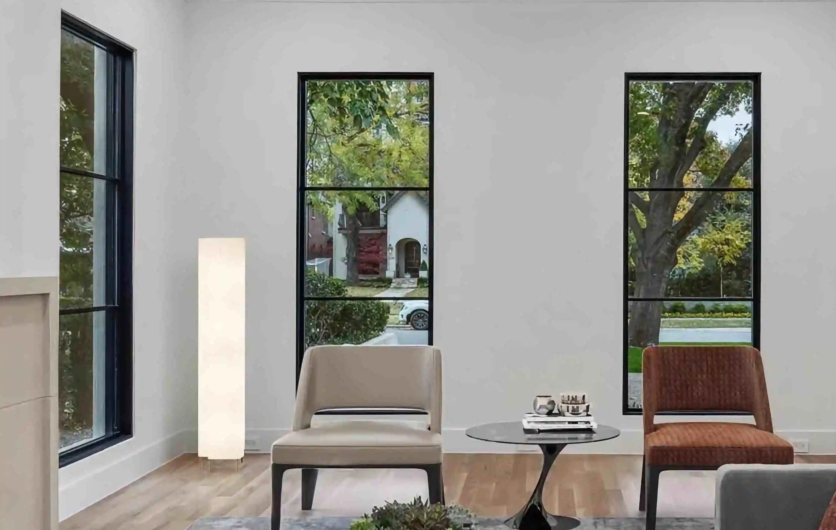 in the living room of a modern home, looking over furniture to a 3 large glass and black iron windows looking over the back yard