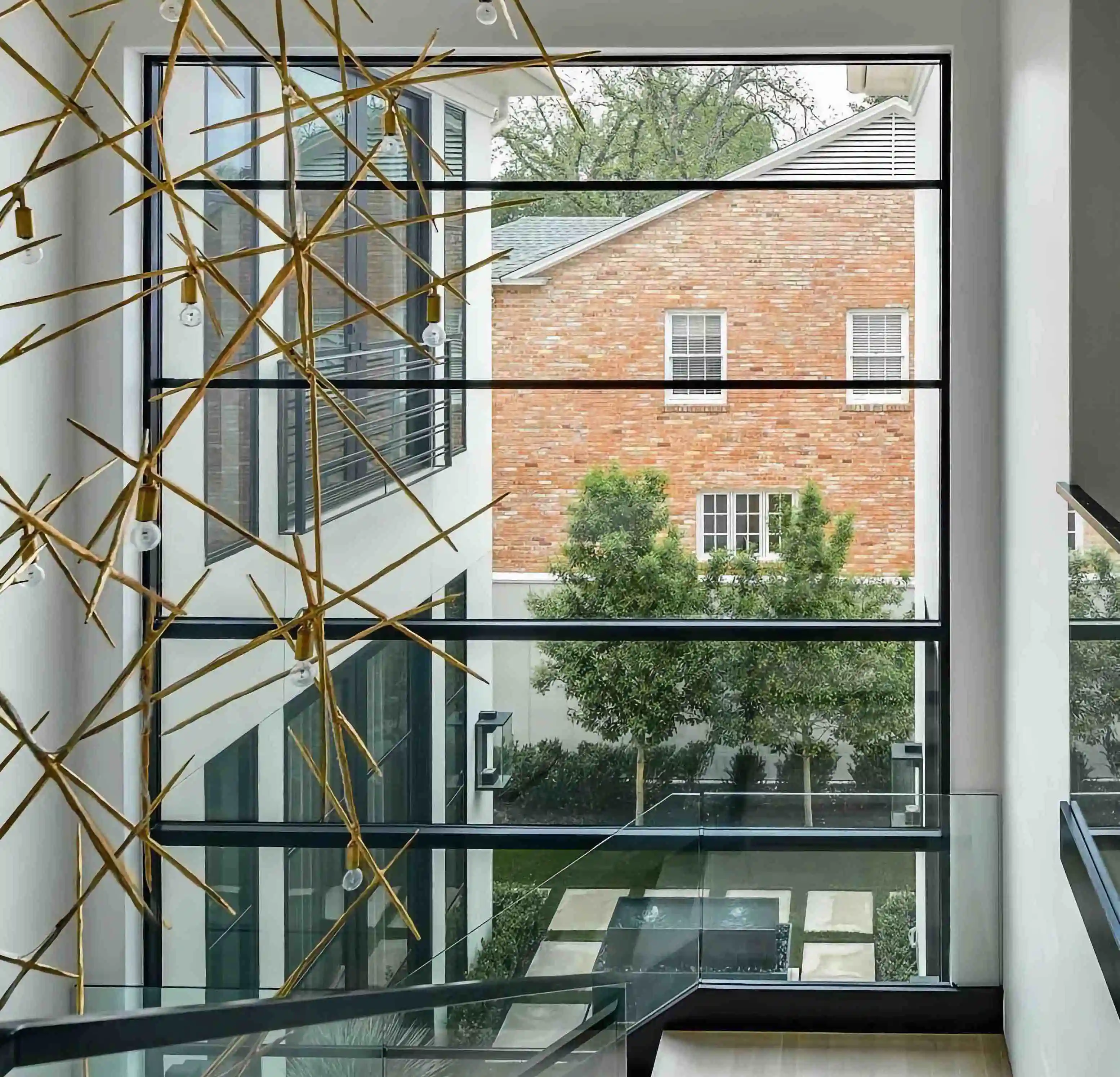 in the living room of a modern home, looking over furniture to a large glass and black iron wall looking over the back yard