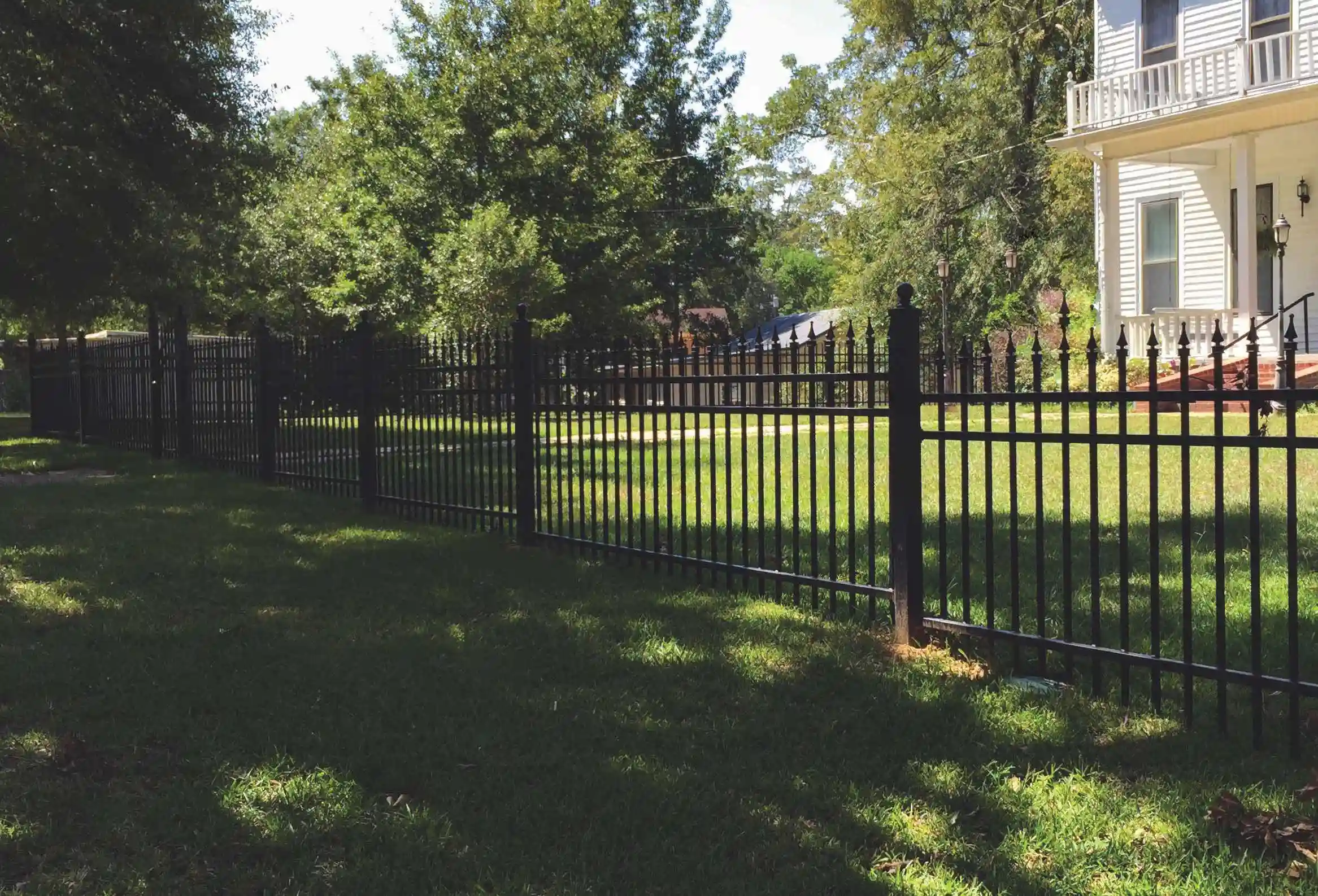 a black iron fence with pointed tops and a house behind it