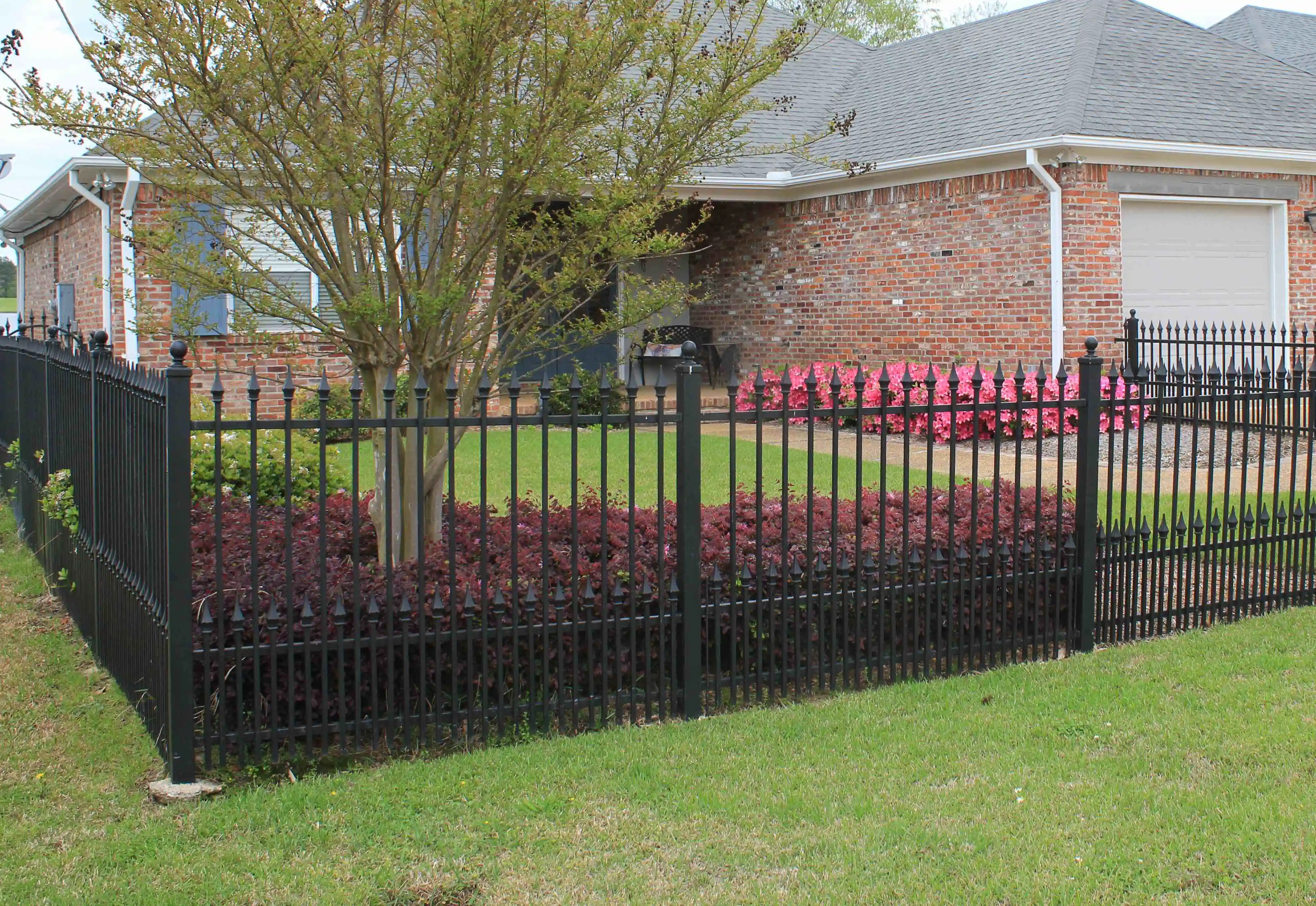 a black iron fence with pointed tops and a house behind it