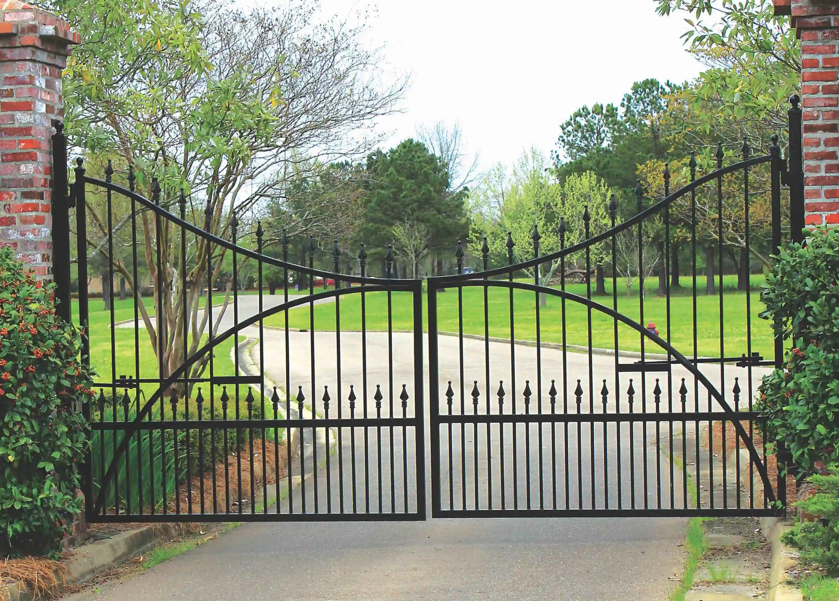 a large black iron gate in the middle of a long driveway leading to a home