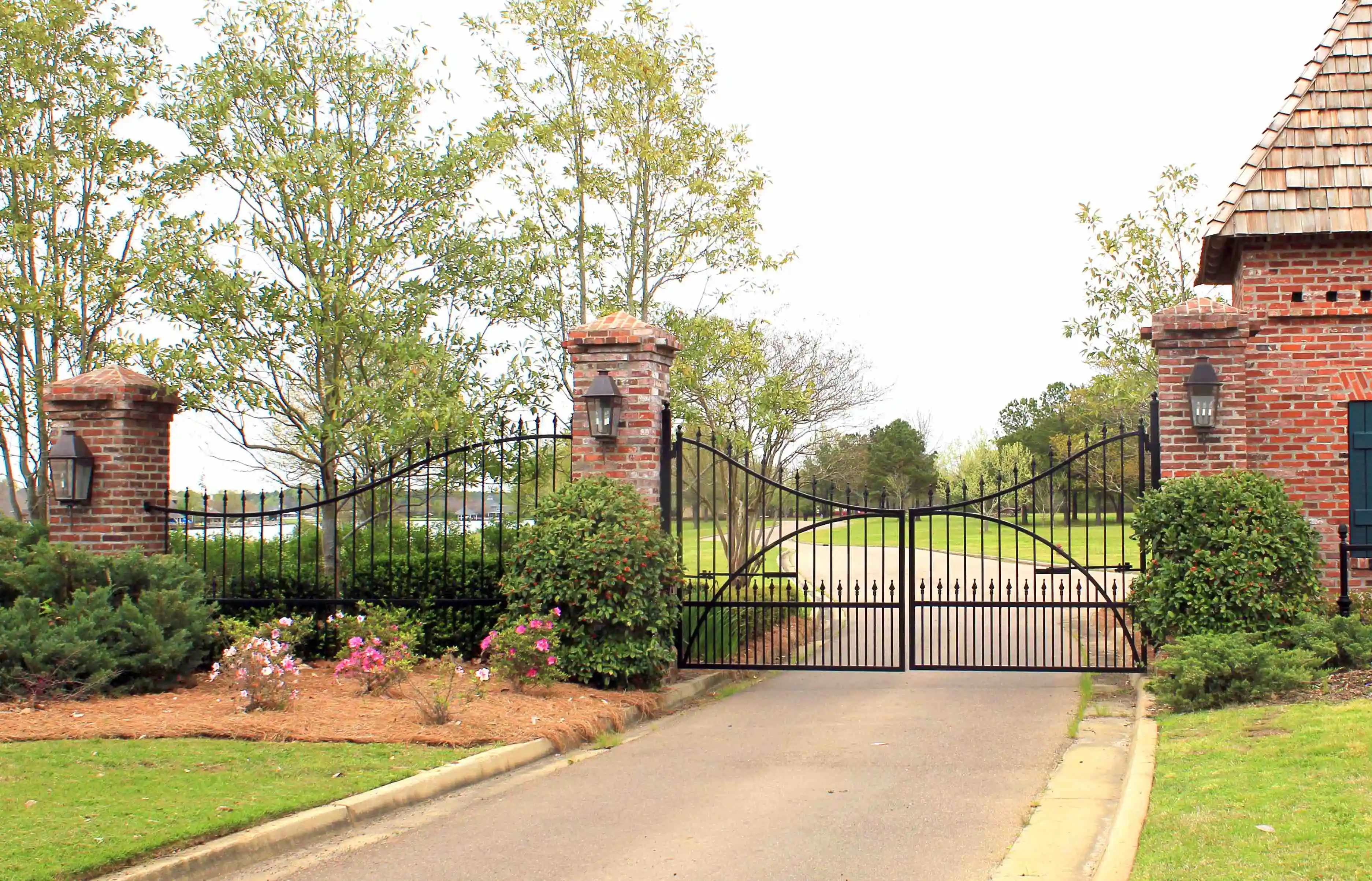 a grand black iron gate with red brick posts at each end viewed from down the concrete driveway 
