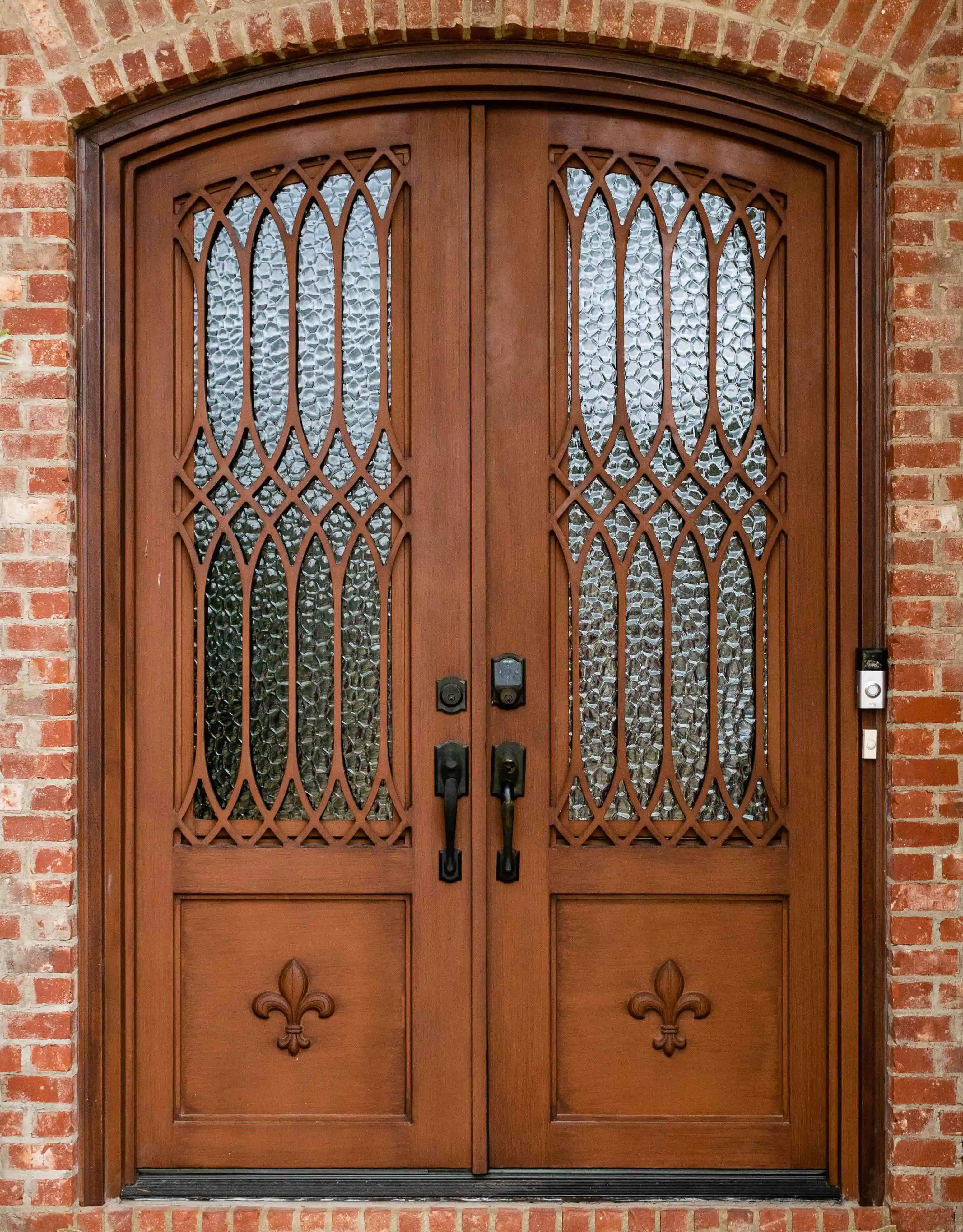an iron double door made to look like dark wood with large panes of glass on each door with intricate black iron swirls on each