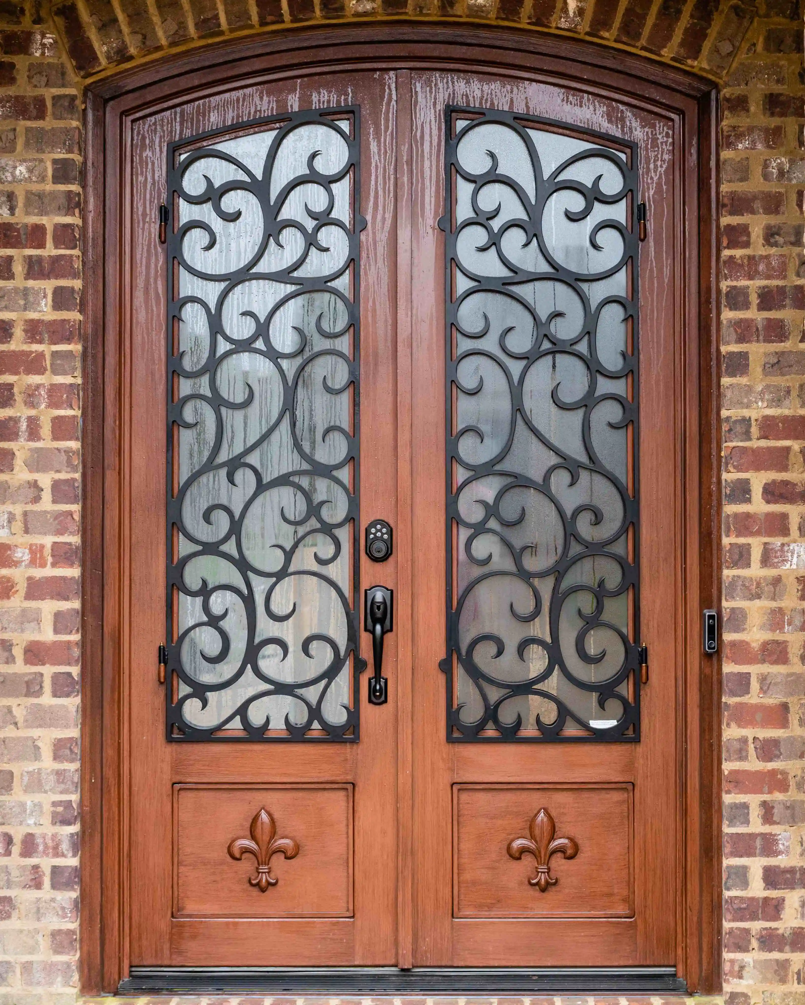 an iron double door made to look like dark wood with large panes of glass on each door with intricate black iron swirls on each
