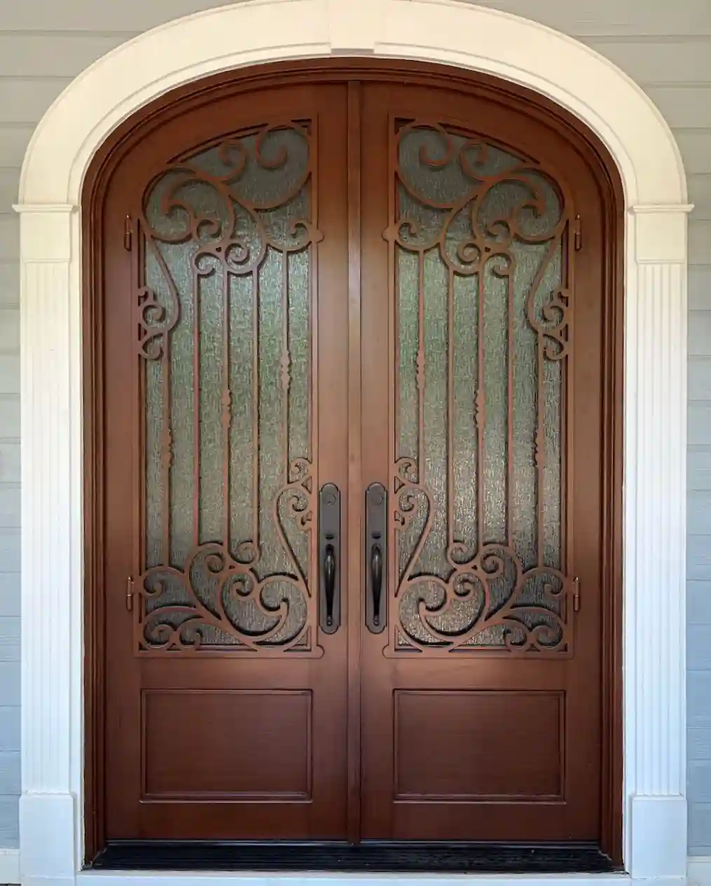 an iron double door made to look like dark wood with large panes of glass on each door with intricate black iron swirls on each