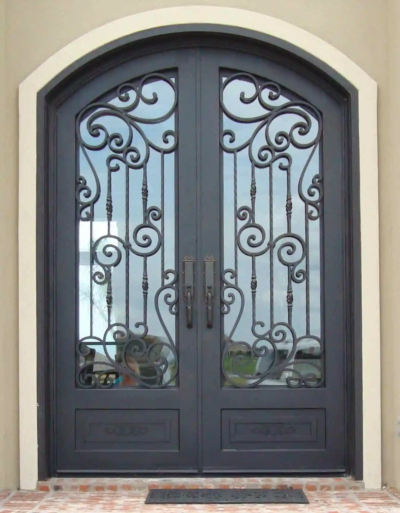 a black iron double door with large panes of glass on each door with intricate black iron swirls on each