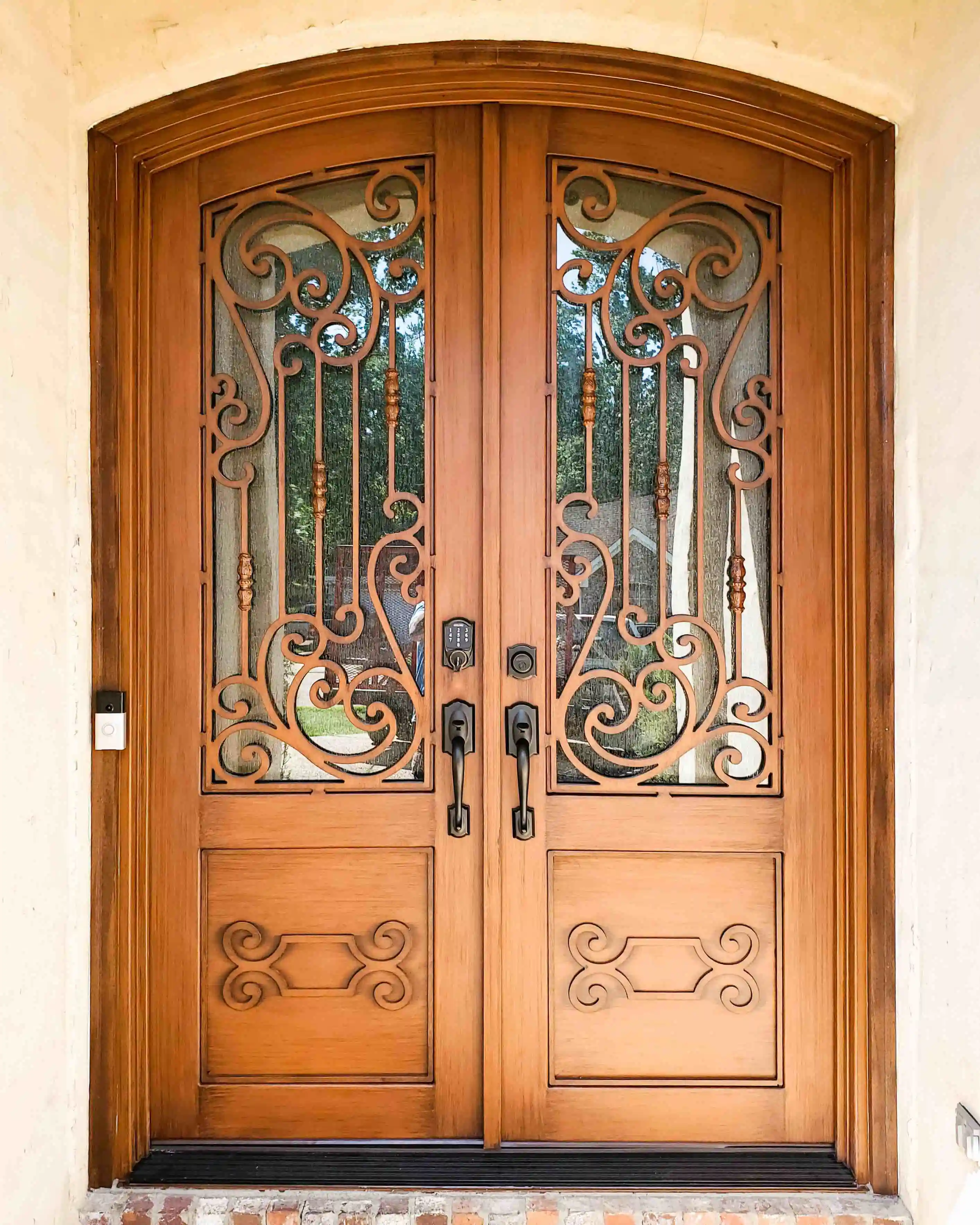 an iron double door made to look like dark wood with large panes of glass on each door with intricate black iron swirls on each